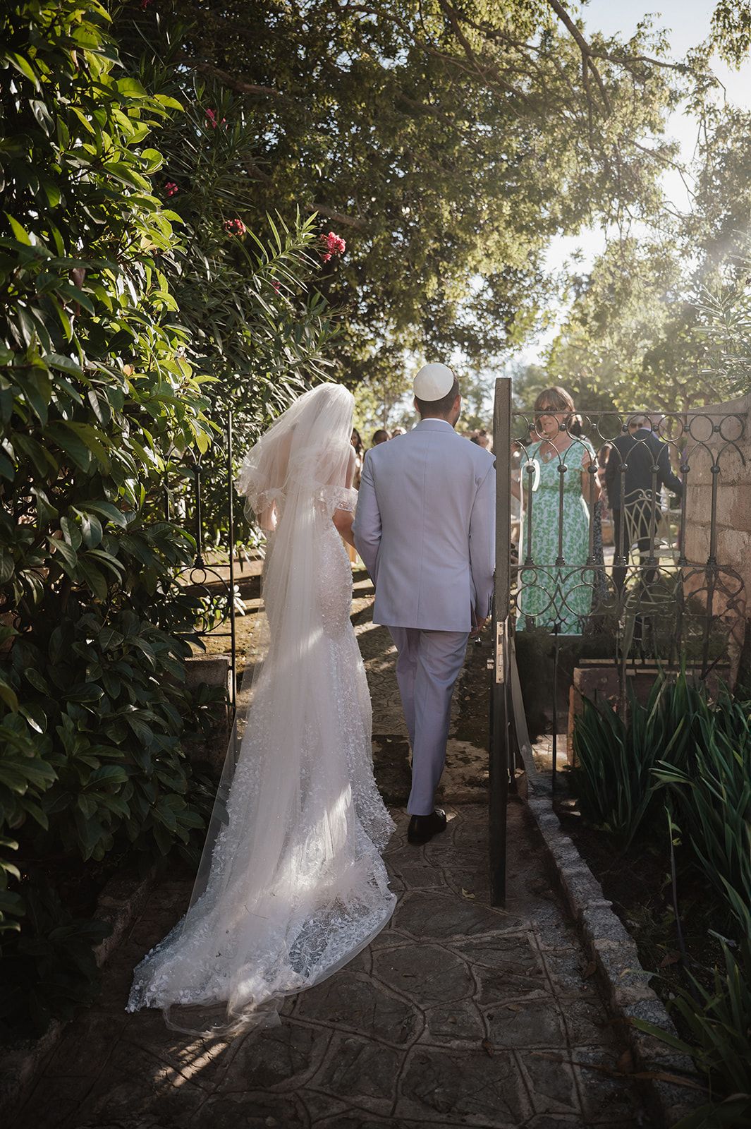 Bride and groom walking hand in hand through sunlit garden path after ceremony.