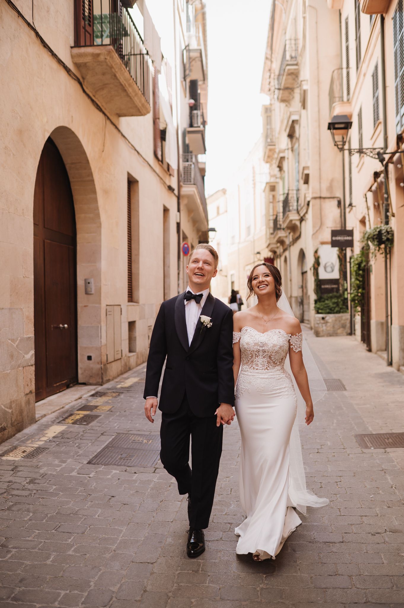 Happy bride and groom walk hand in hand through charming European cobblestone street.