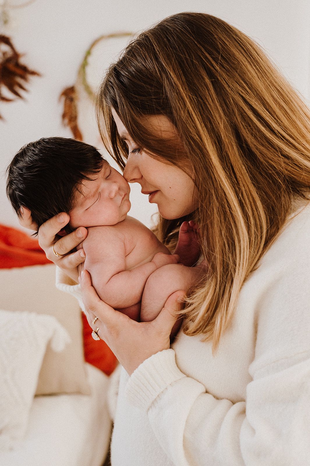A mother tenderly holds her newborn baby close to her face, sharing an intimate moment in a warm, softly lit setting.