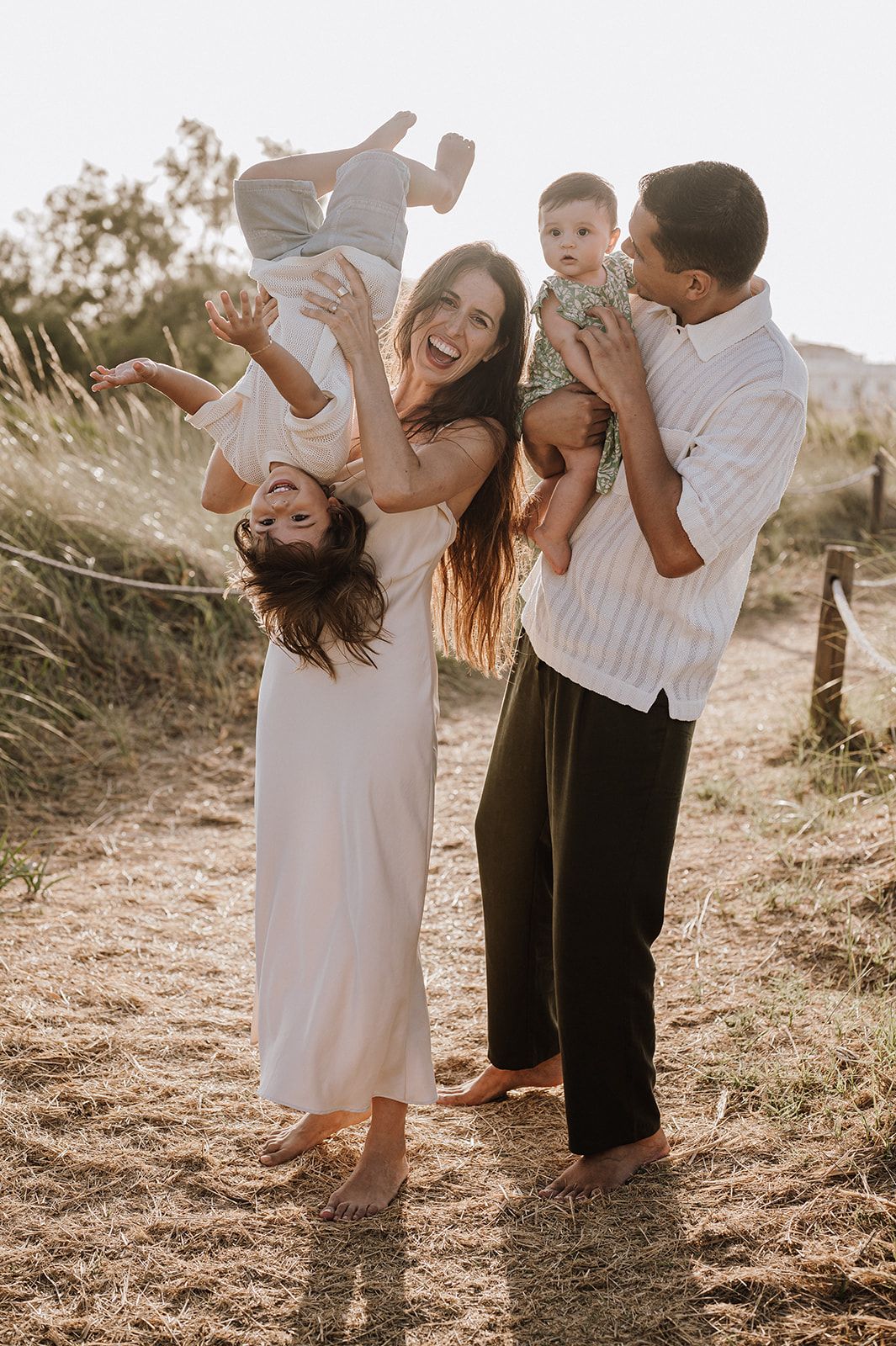 Joyful family of four playing outdoors in golden hour light on a coastal pathway.