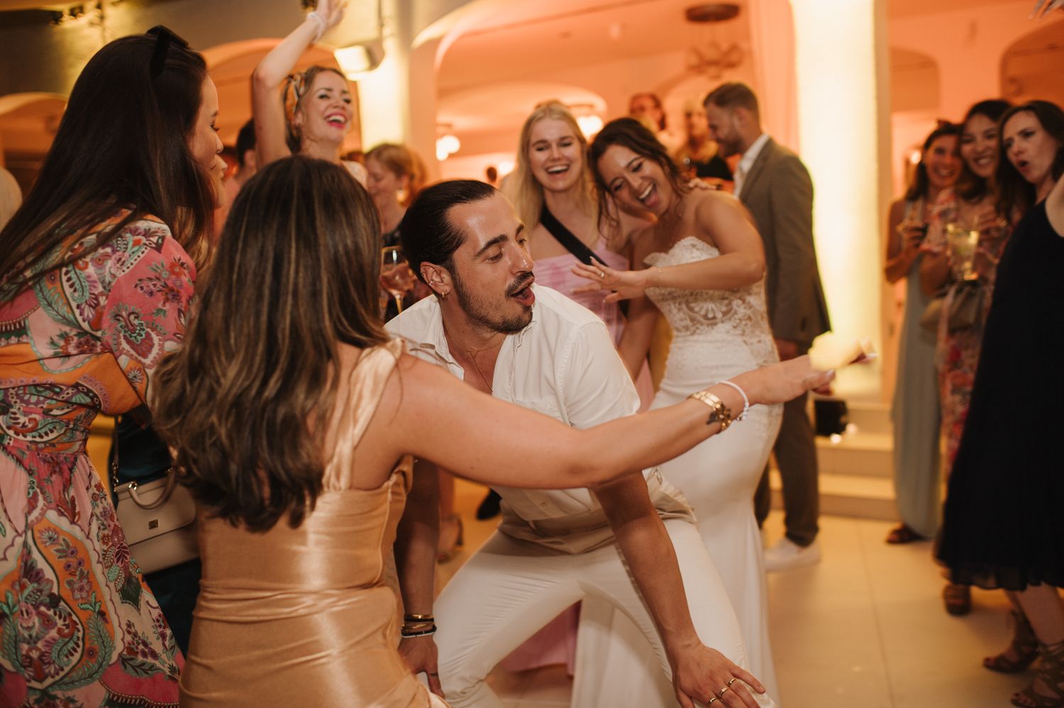 Energetic wedding guests dance together on the dance floor during a lively reception celebration.