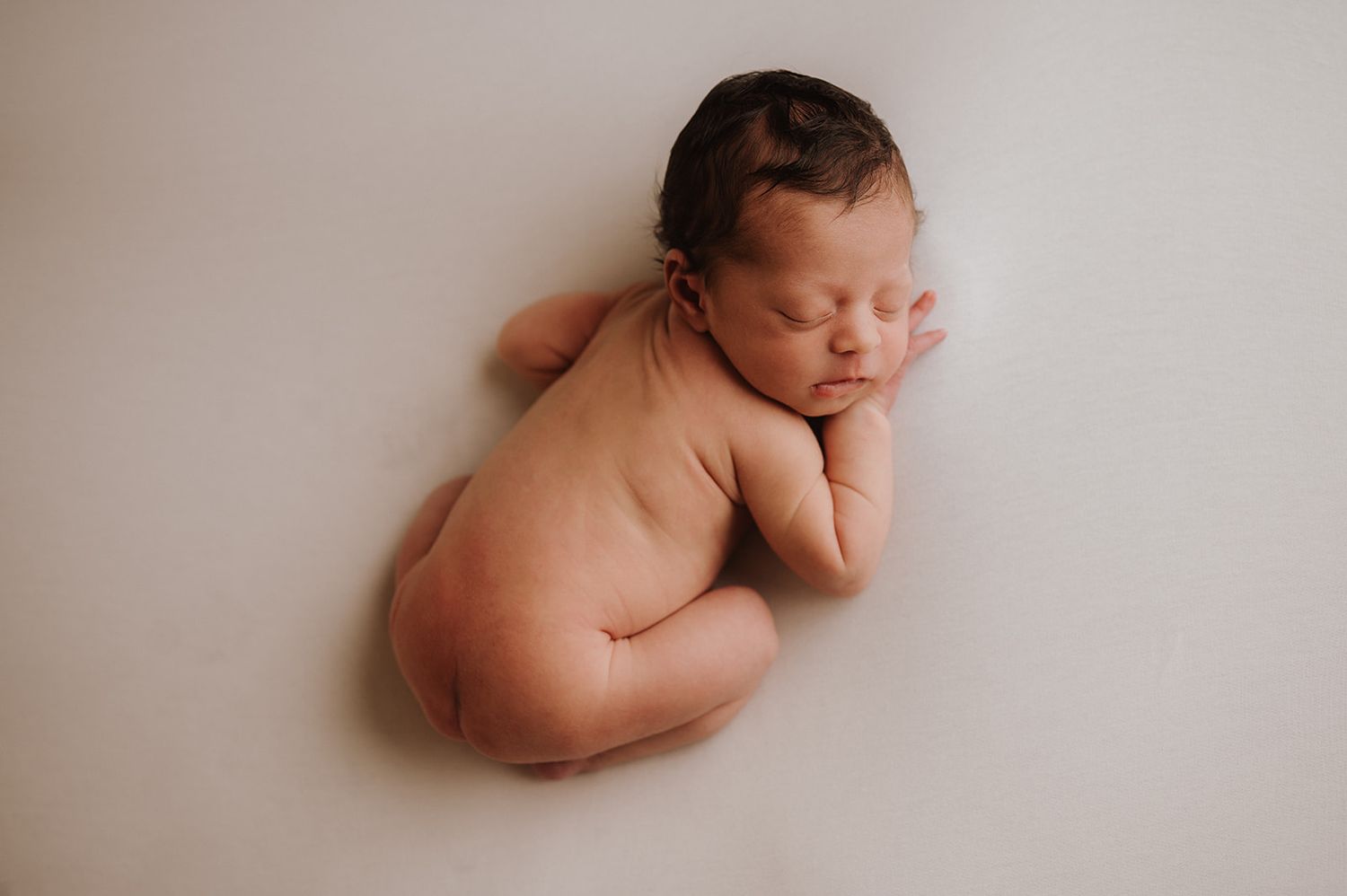 Peaceful newborn baby sleeping curled up on a soft white background in a classic posed newborn photo.
