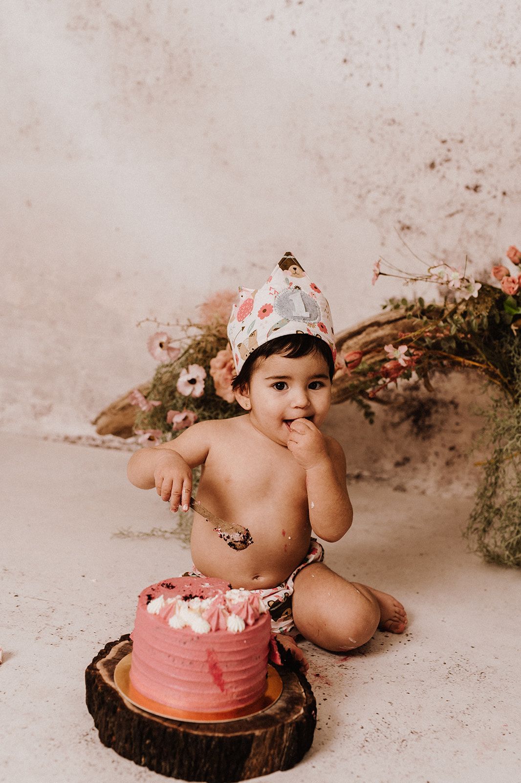 Baby girl in birthday crown smashes pink ombre cake during first birthday cake smash photo session.