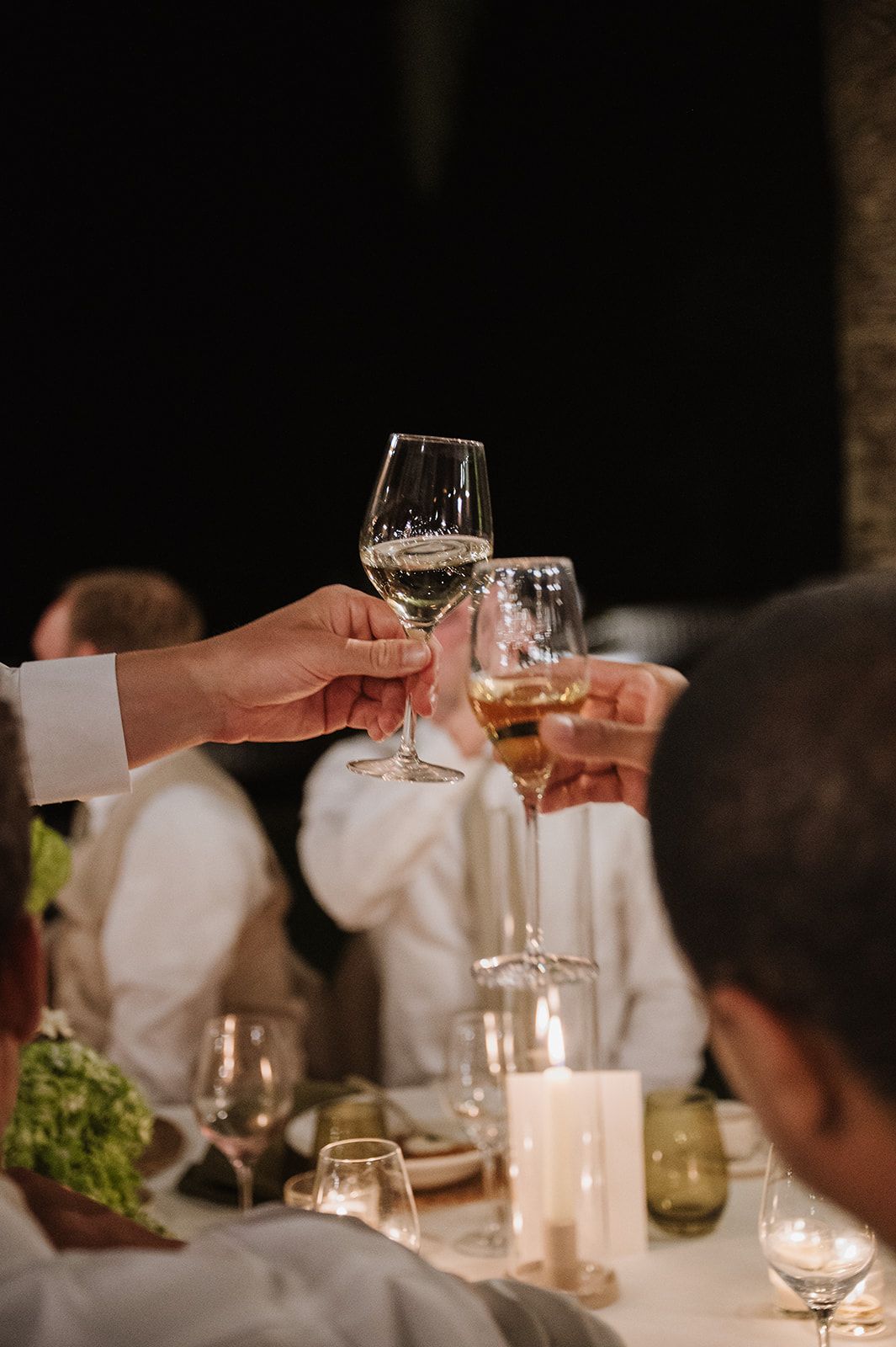 Guests clinking wine glasses in candlelit toast at elegant wedding reception dinner table.