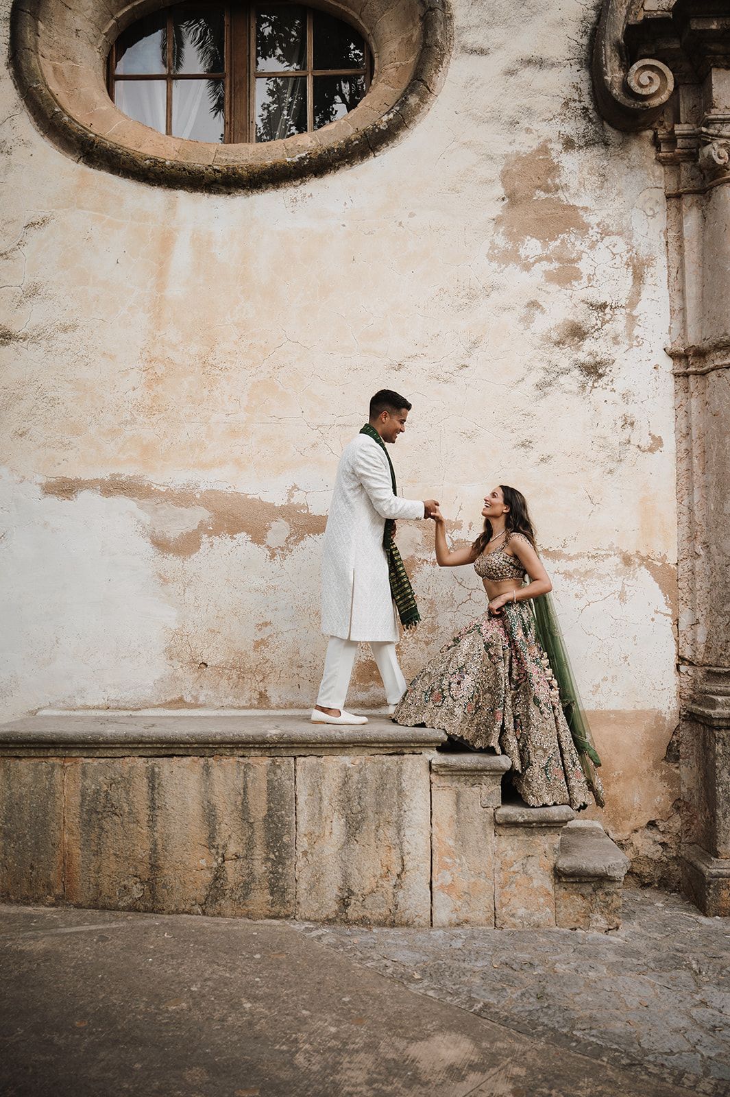 Indian couple in traditional wedding attire hold hands on stone steps in Jardines de Alfabia Mallorca