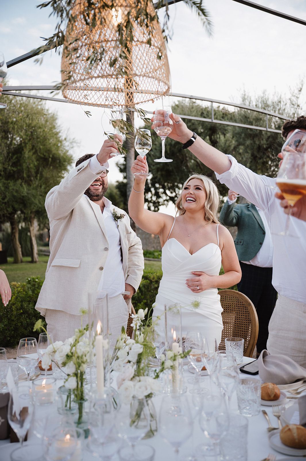 Bride and groom toast with wine glasses at an elegant outdoor wedding reception with floral centerpieces.