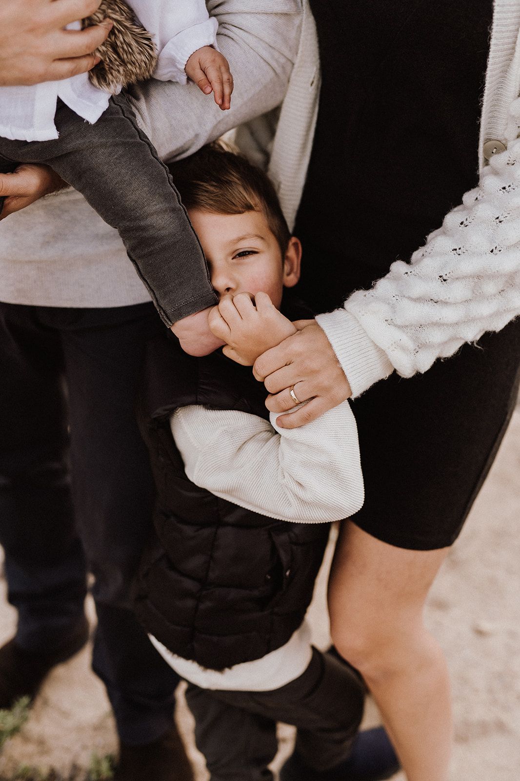 A young boy playfully hides his face between his parents during a casual family photo session outdoors.