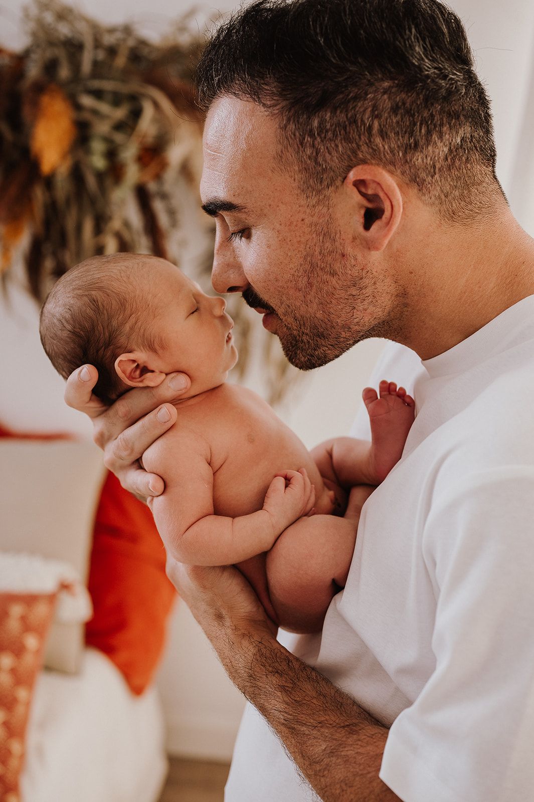 A father tenderly holds his newborn baby close, smiling lovingly in a warm, decorated room.