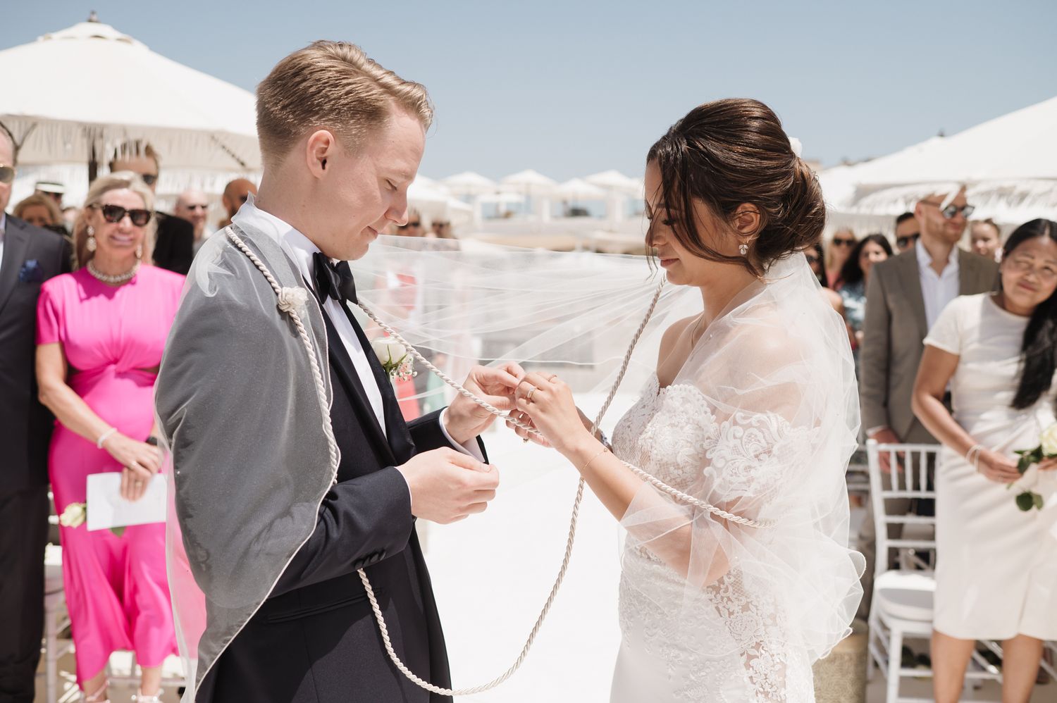 Bride and groom exchange rings during outdoor beach wedding ceremony on sunny day.