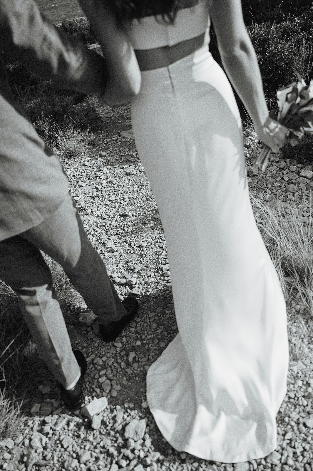 Close-up of bride in elegant white wedding gown walking on a gravel path.