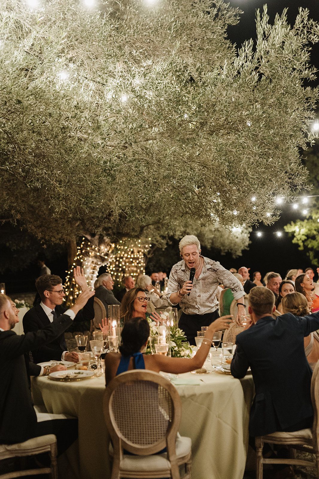 Wedding guests celebrate under olive trees with string lights during an outdoor night reception.