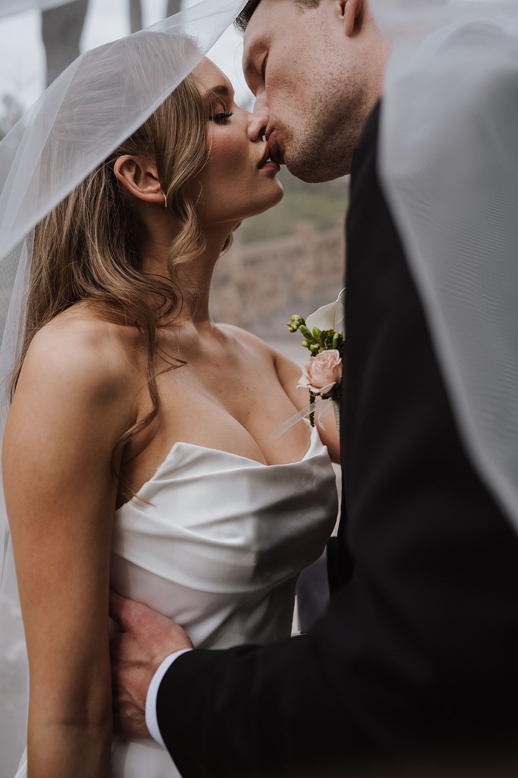 Bride and groom sharing a kiss under bridal veil in intimate close-up wedding portrait.
