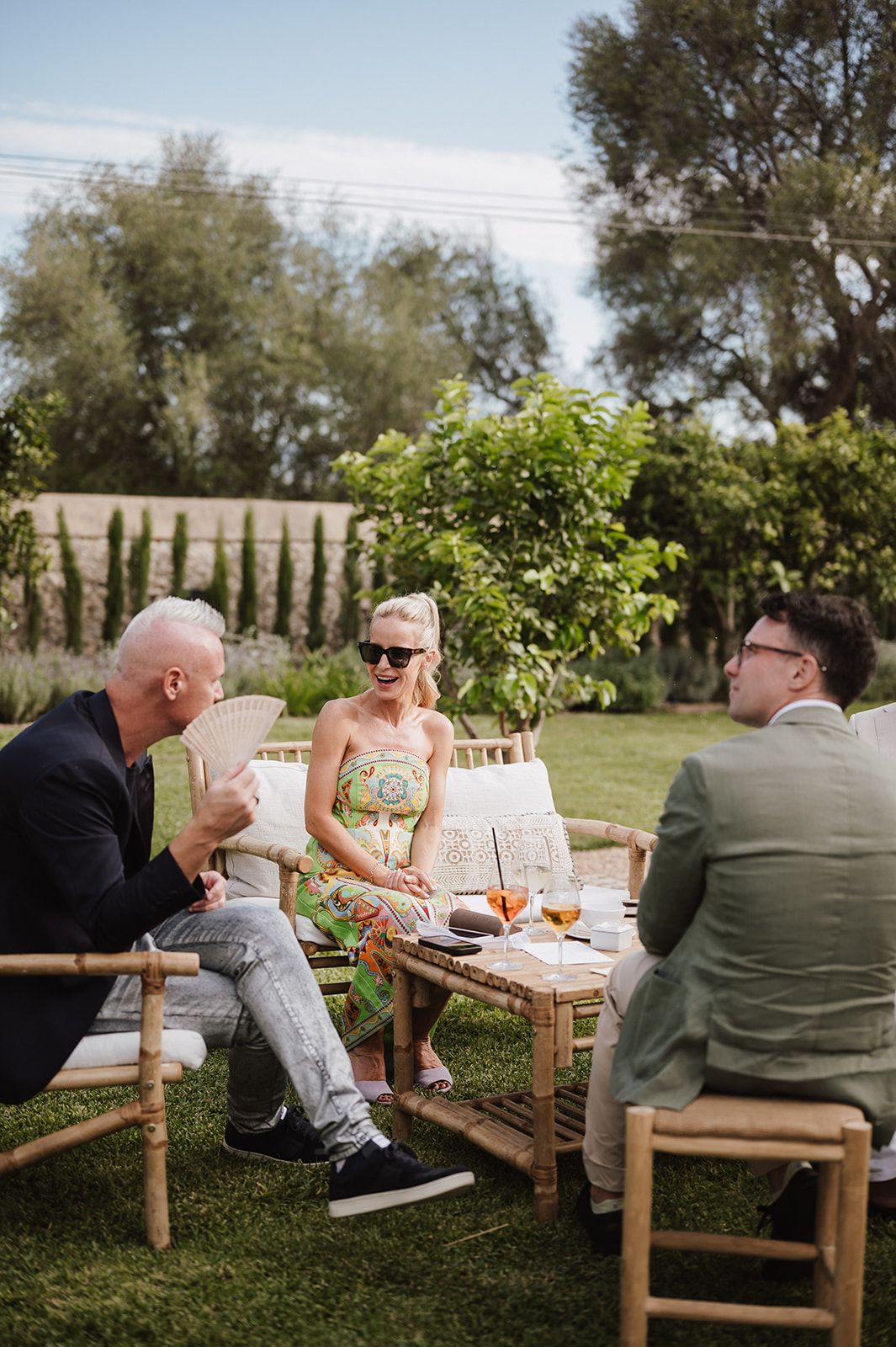 Wedding guests relaxing on garden furniture chatting during outdoor cocktail hour reception.