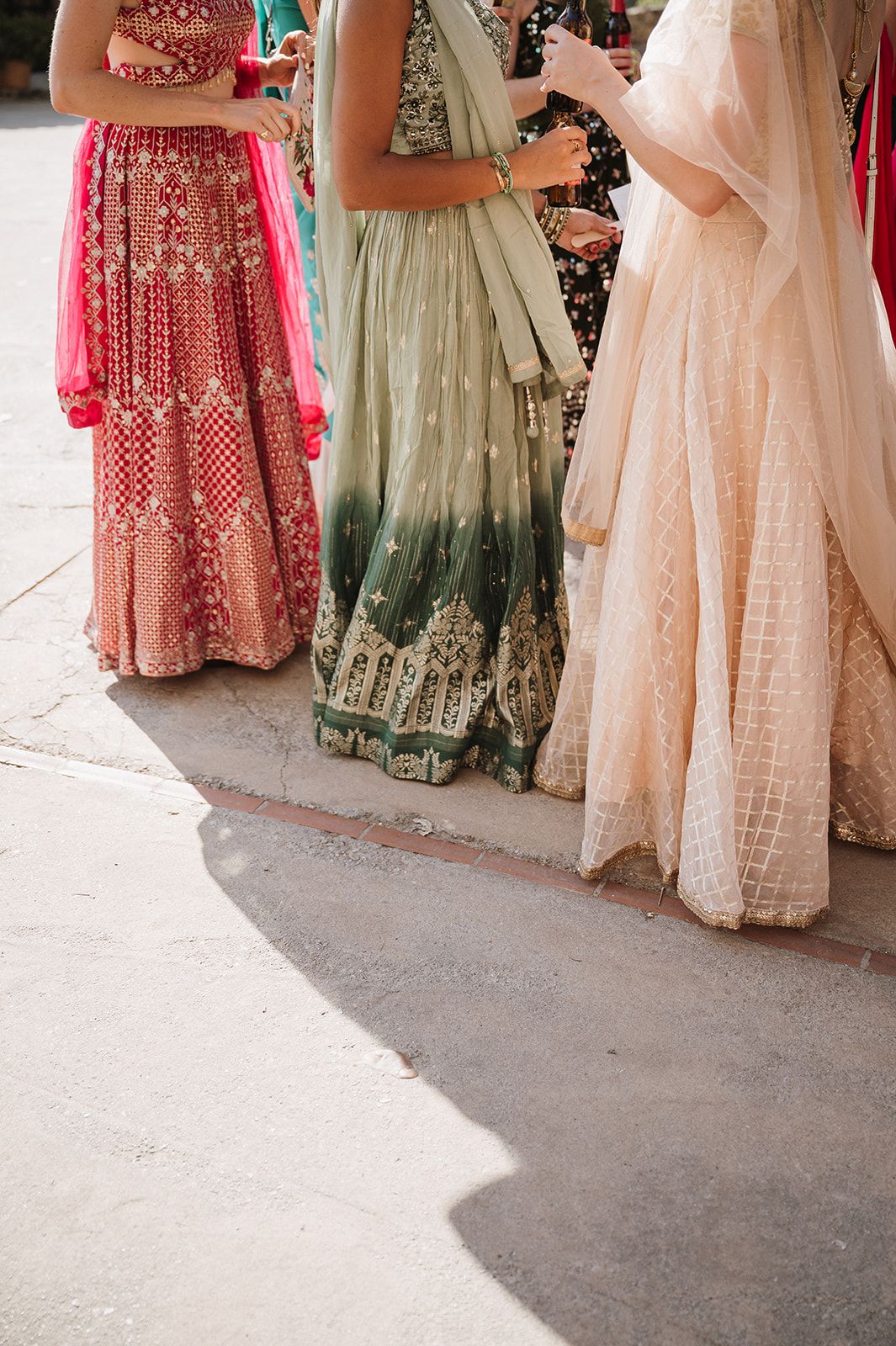Women in colorful Indian lehengas including pink and sage green with floral embroidery at a wedding.