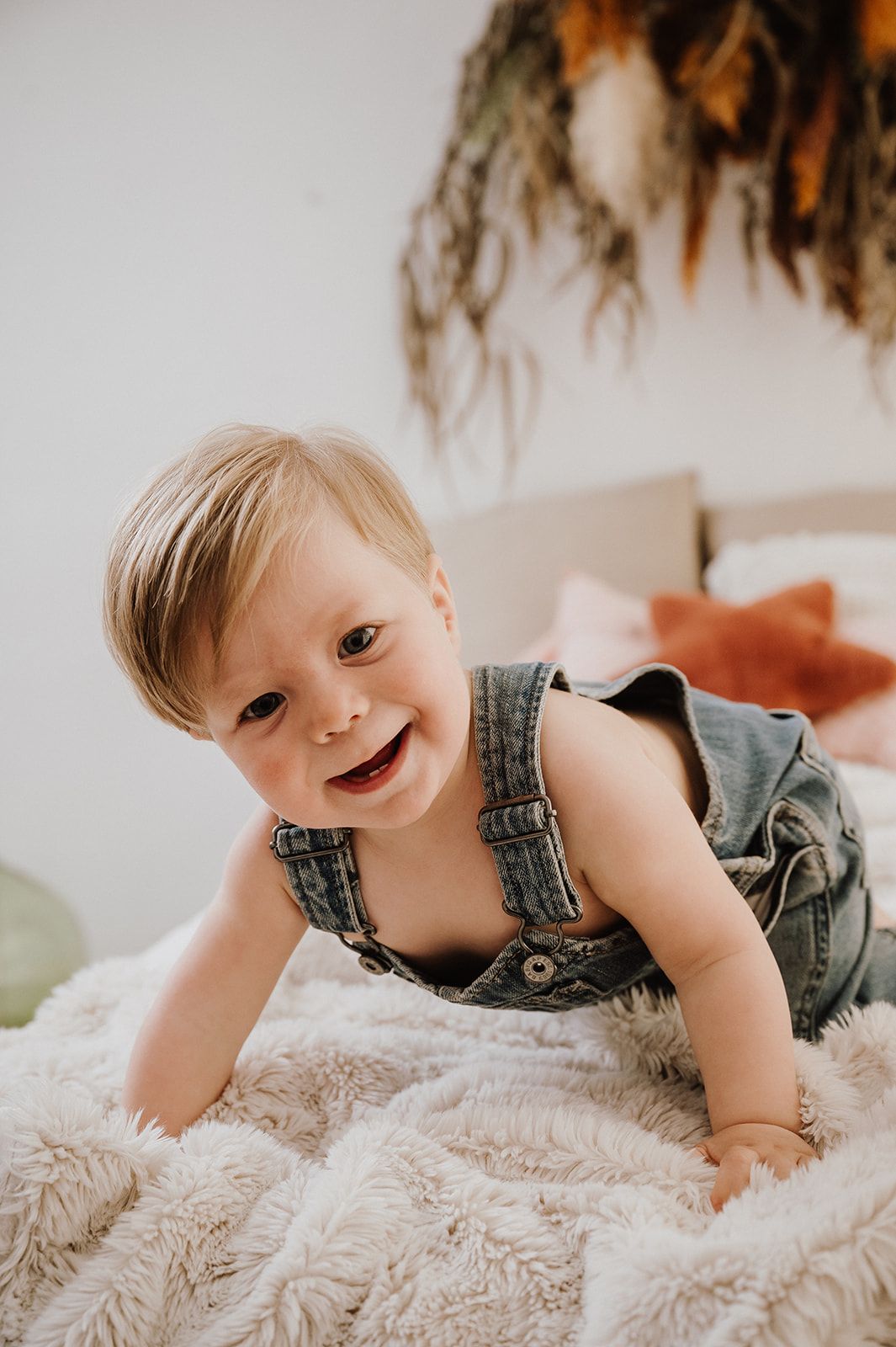 Smiling baby in denim overalls crawling on a fluffy white blanket.