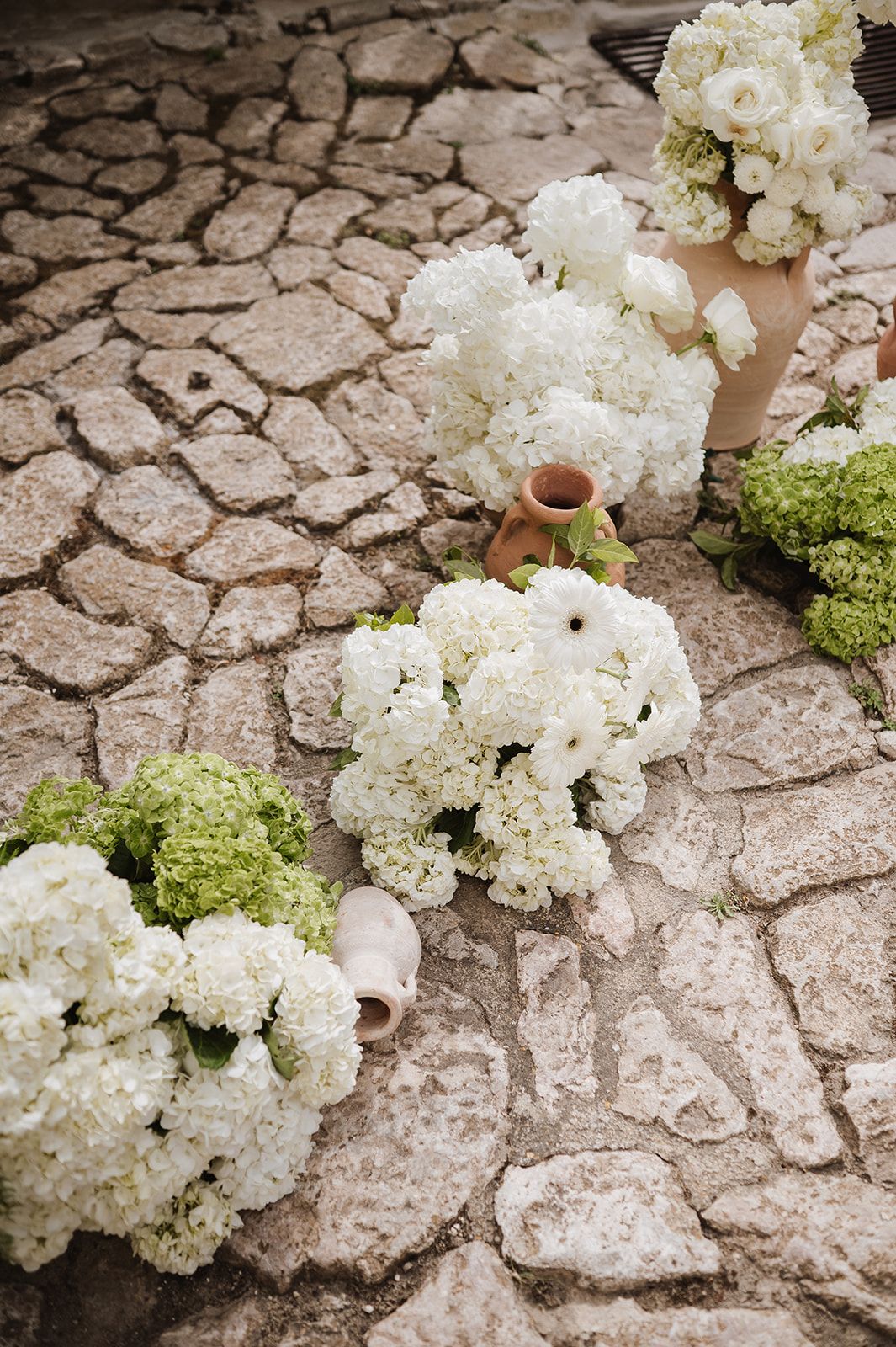 White hydrangea and green flower arrangements in terracotta vases displayed on rustic cobblestone.