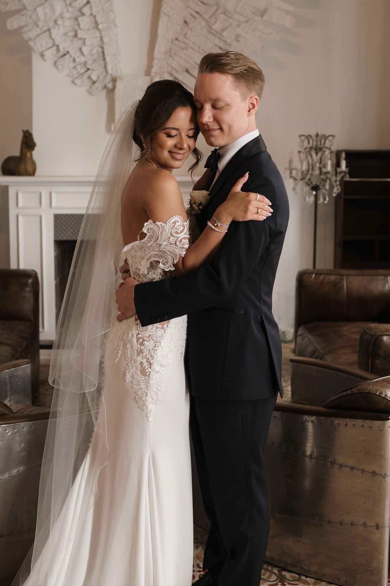 Bride and groom share tender embrace indoors on wedding day.