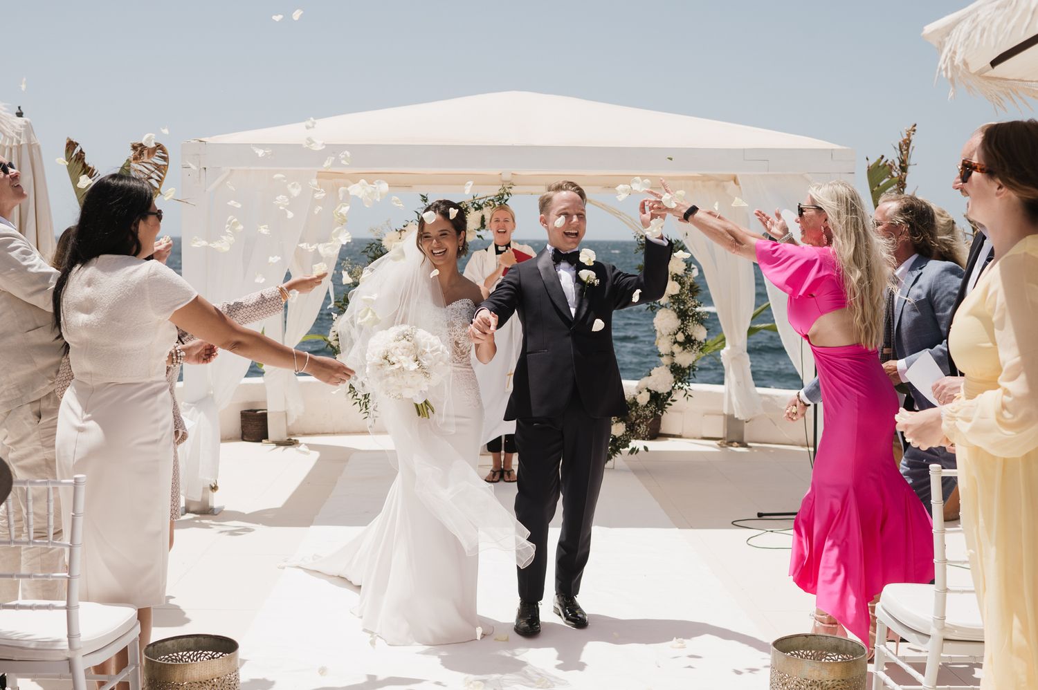 Joyful newlyweds walking down the aisle as guests shower them with white confetti outdoors.
