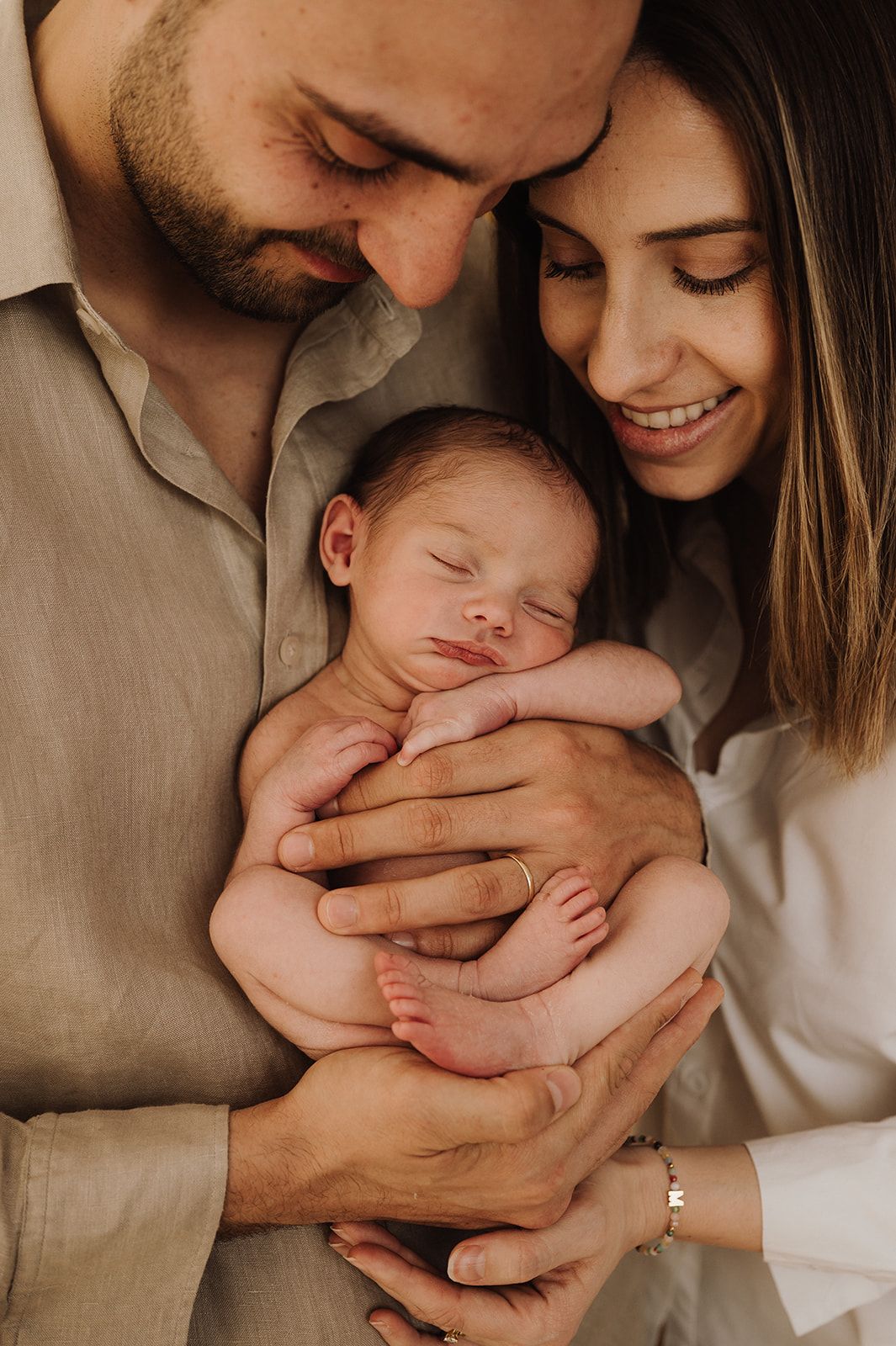 New parents tenderly cradle their sleeping newborn baby together in a warm, intimate family portrait.