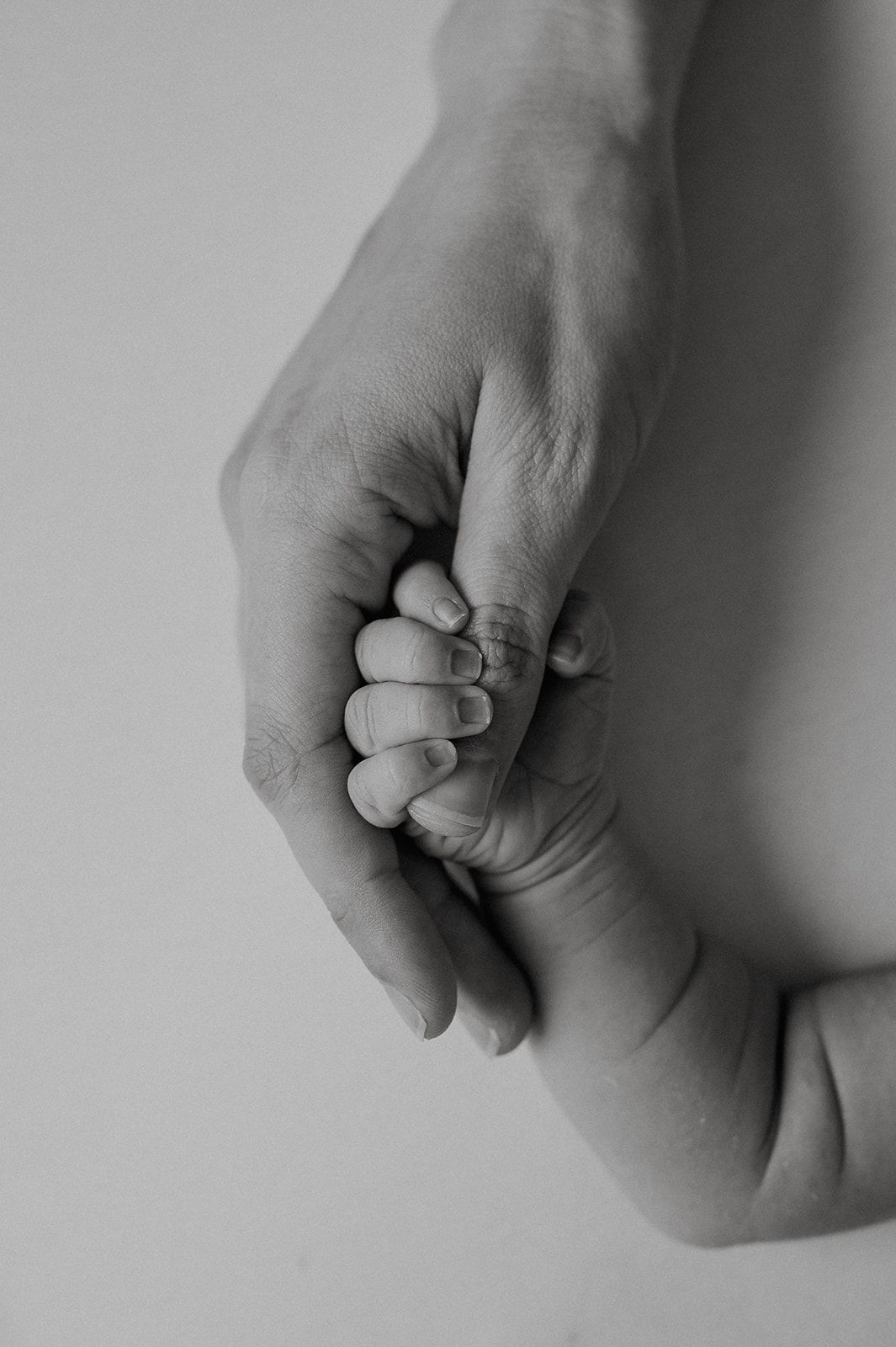 Black and white photo of an adult hand gently holding a newborn baby's tiny fist, symbolizing love and new life.