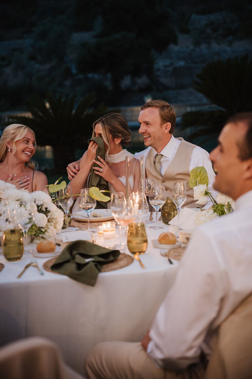 Bride and groom share an intimate moment at candlelit outdoor wedding reception dinner table at dusk.