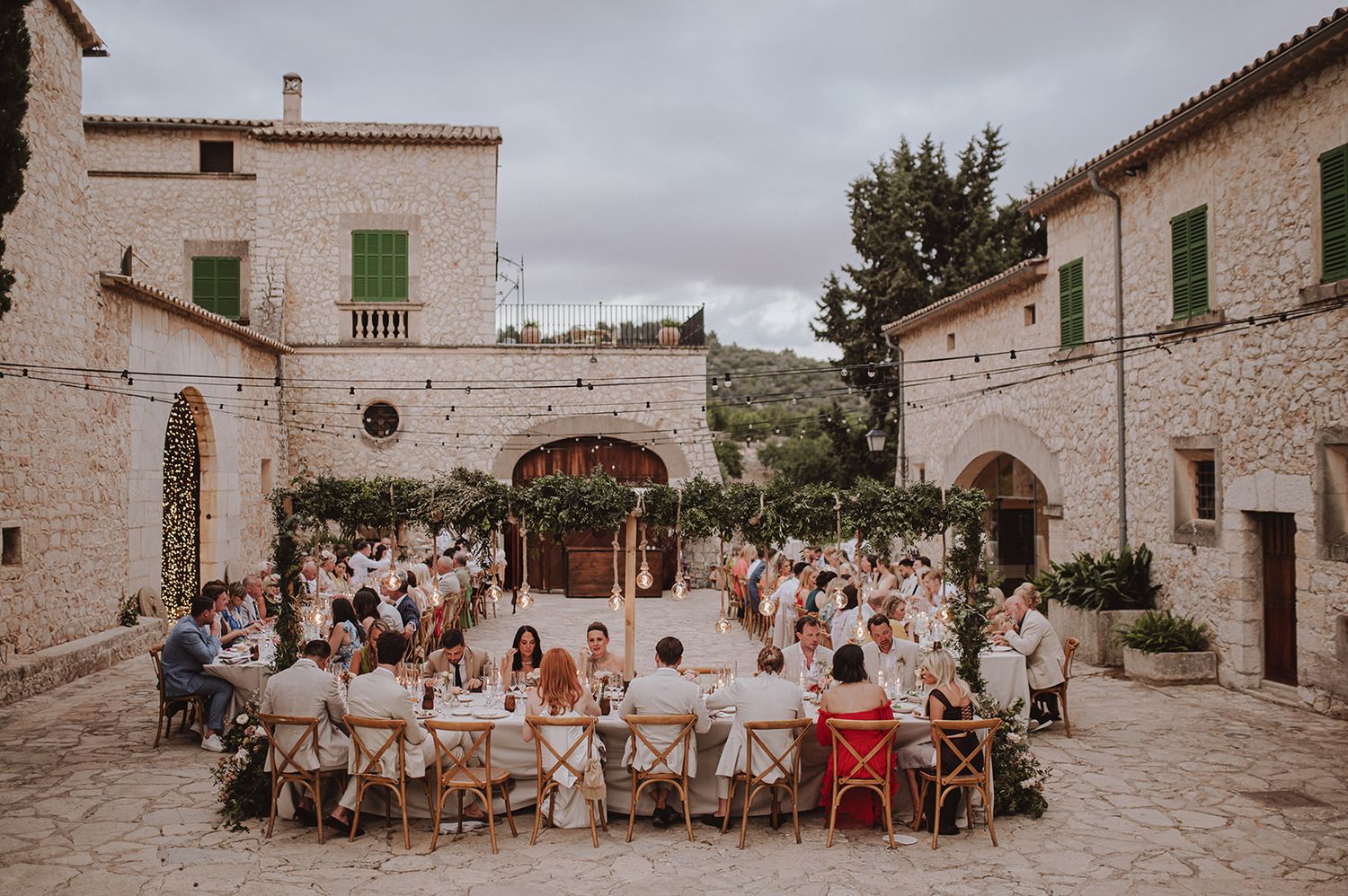 Outdoor wedding reception in a rustic stone courtyard with guests seated at decorated tables.
