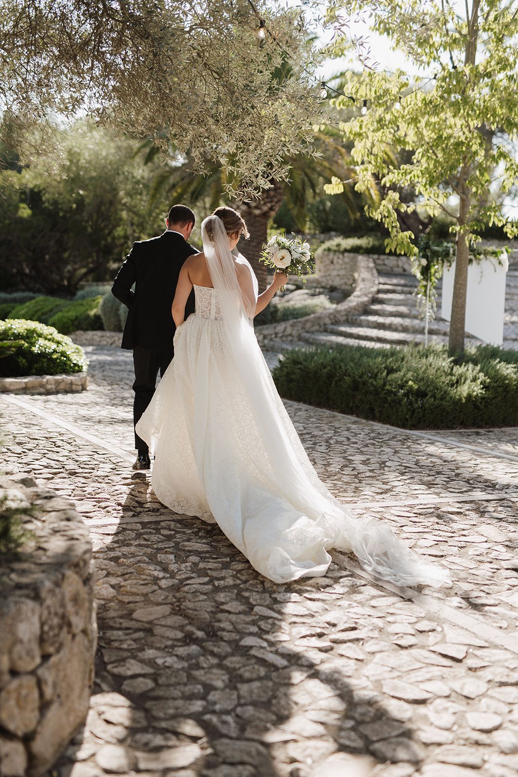Bride and groom walk hand in hand along a cobblestone path at their elegant outdoor wedding.