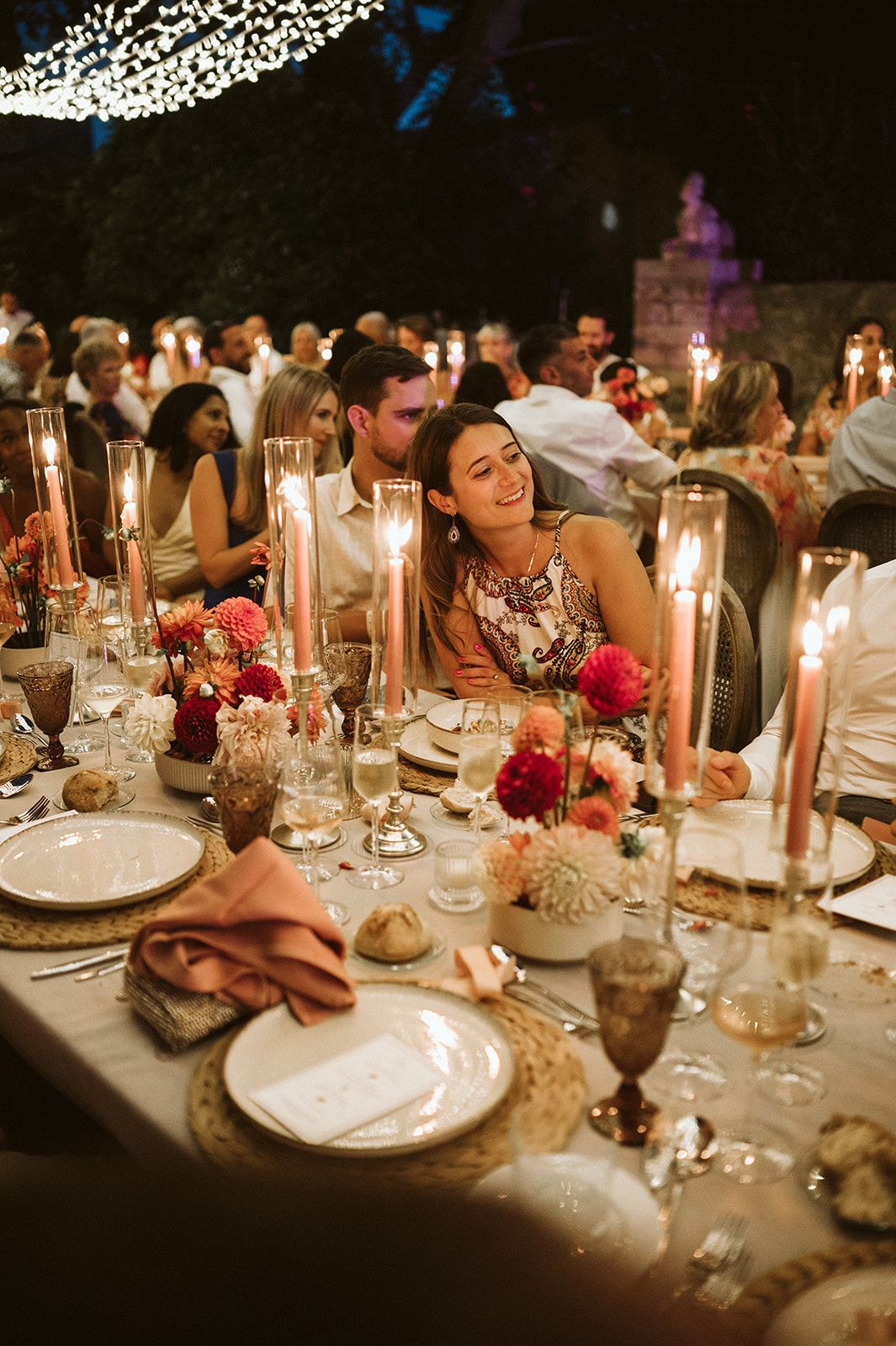 Elegant candlelit wedding reception dinner table adorned with pink tapers and colorful floral arrangements.