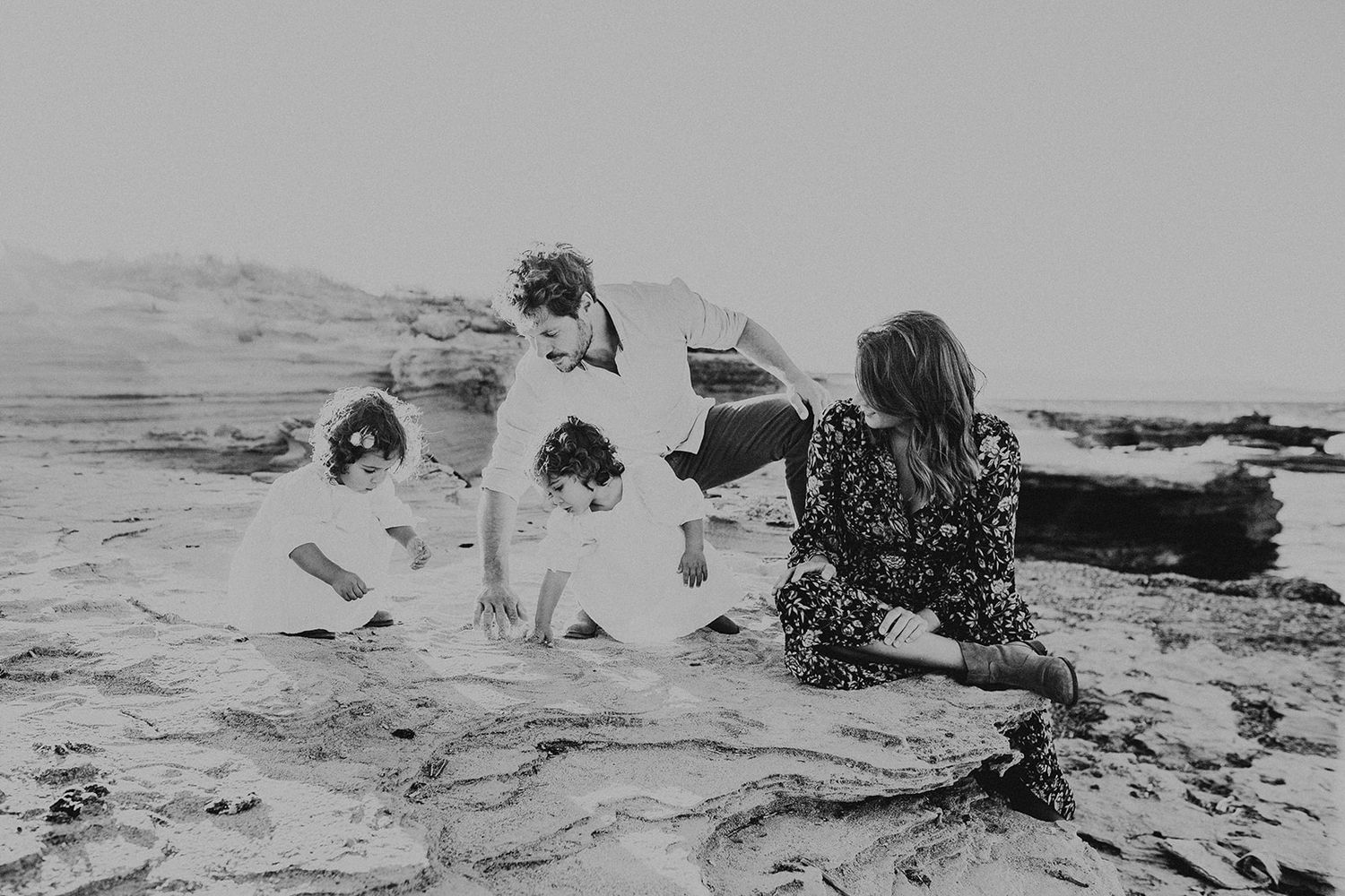 Black and white photo of a family exploring rocky beach together on a cloudy day.