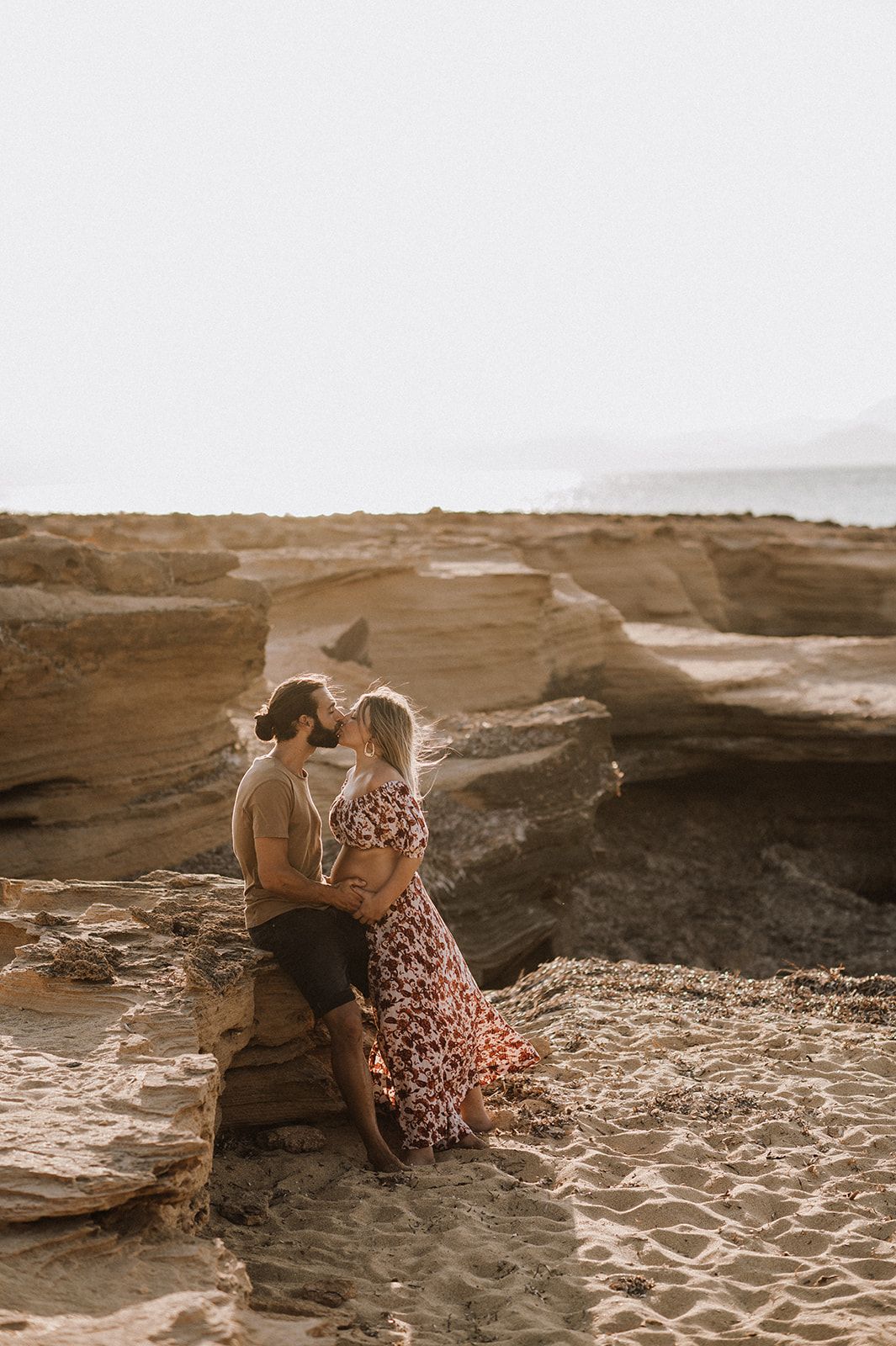 Couple sharing a romantic kiss on golden sandstone cliffs by the ocean during sunset.