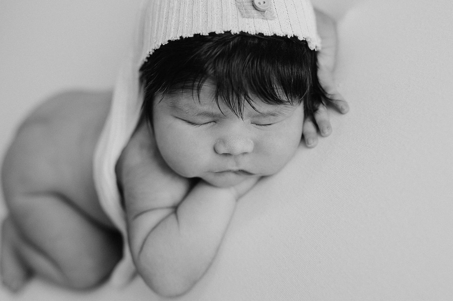 Black and white newborn portrait of a sleeping baby wearing a knit hat, resting peacefully on hands.