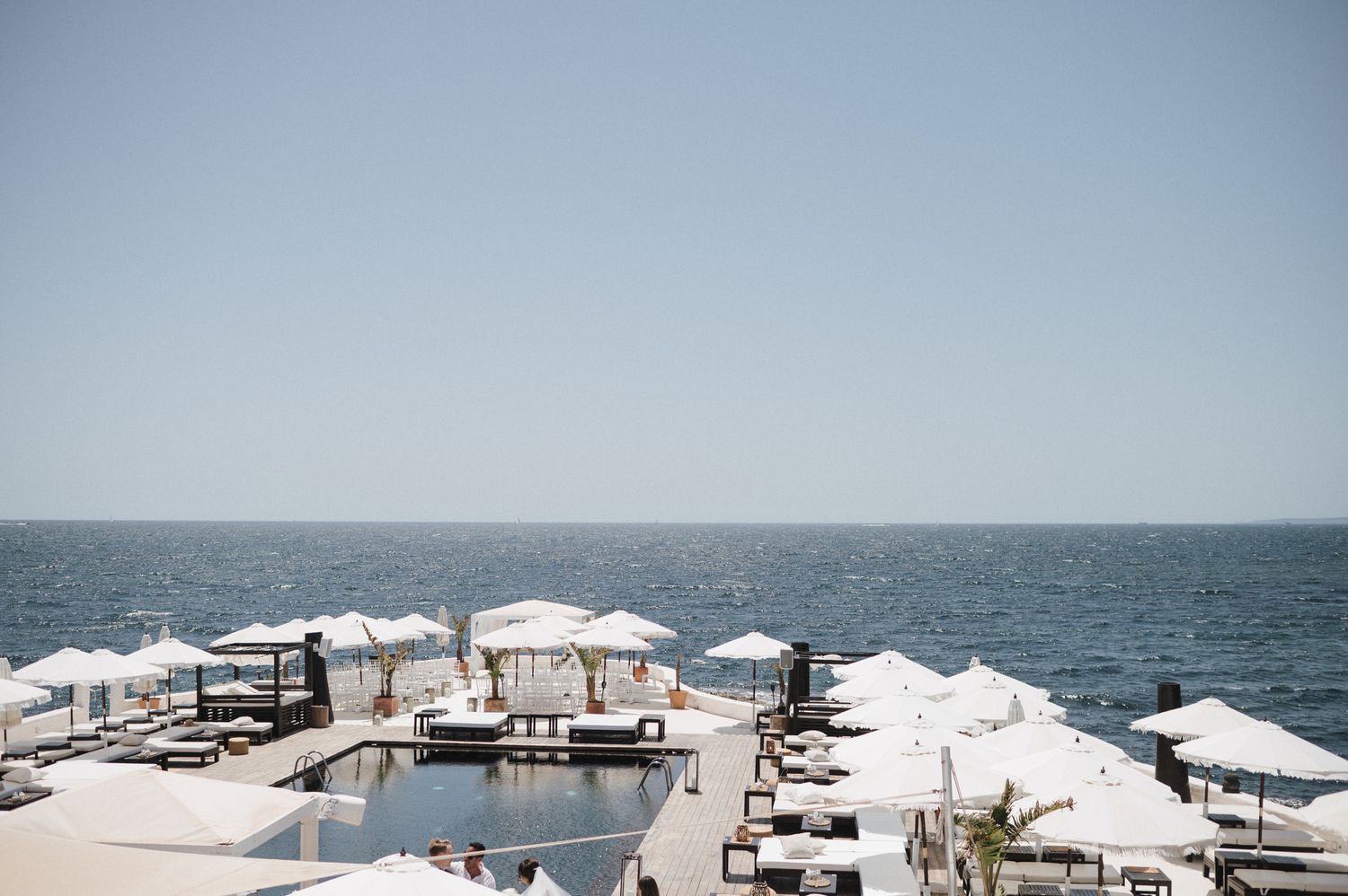 Panoramic view of elegant beachfront wedding venue with white sun umbrellas and infinity pool overlooking the sea.