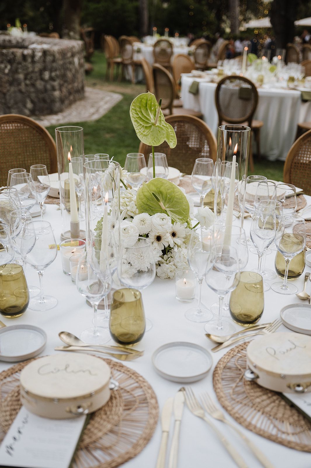 Elegant wedding reception table with white floral centerpieces, green anthurium leaves, and woven chargers.