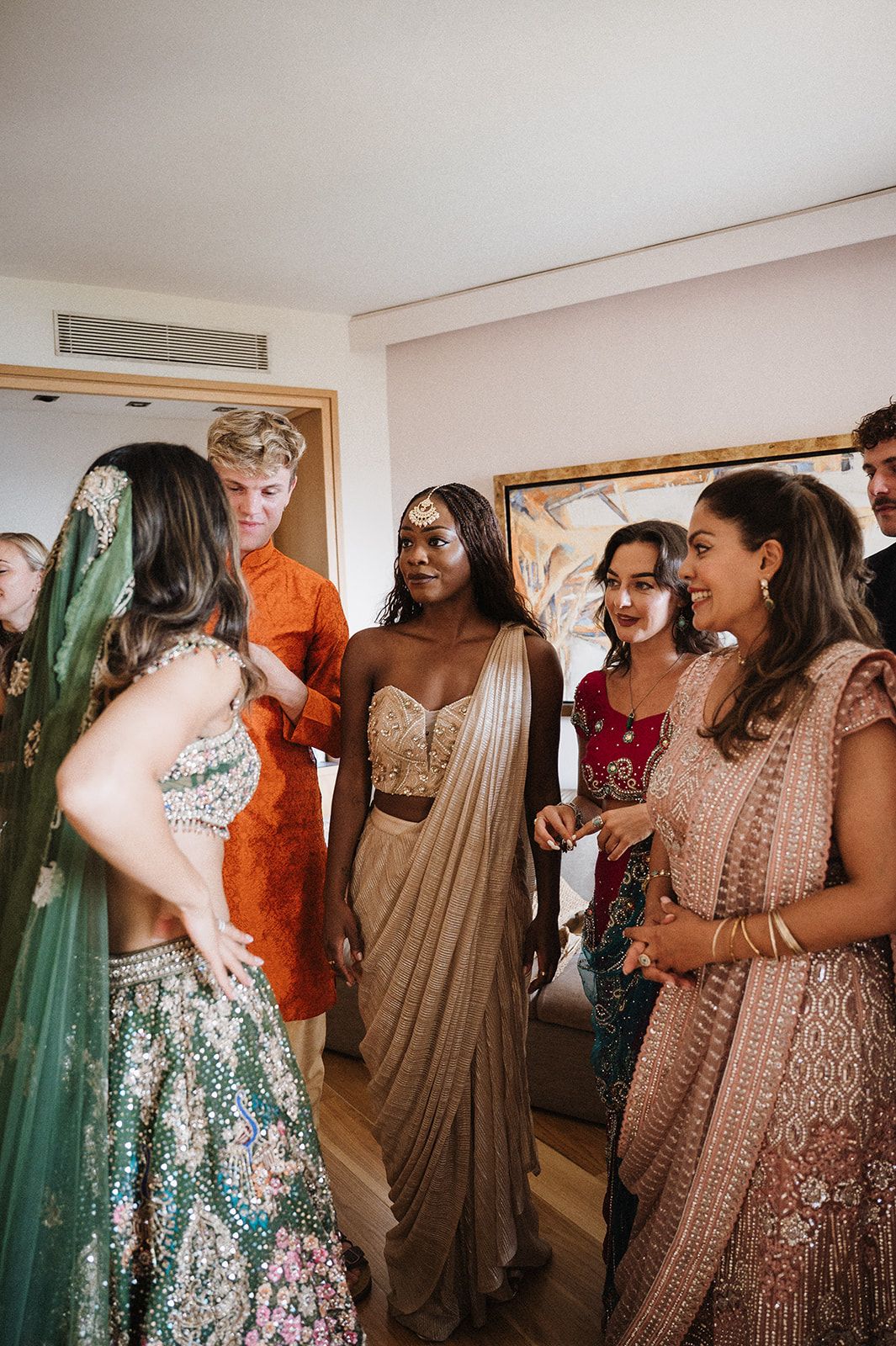 Wedding guests in traditional Indian attire including sarees and lehengas socializing indoors before ceremony.