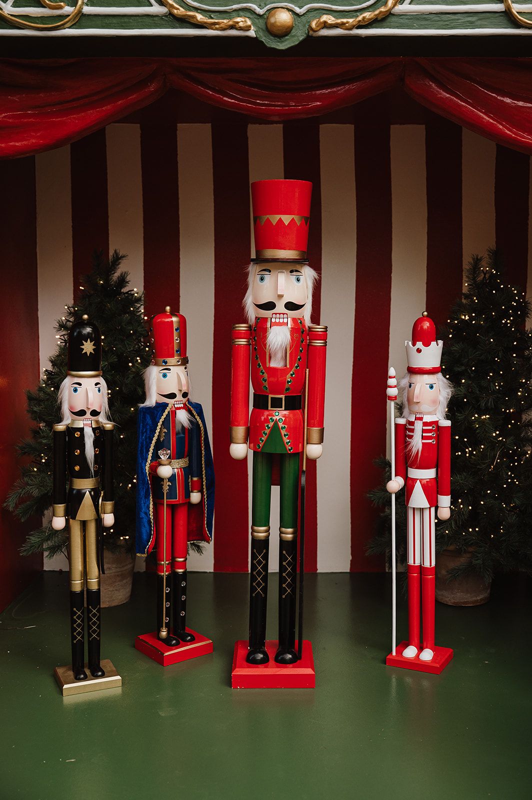 Three decorative Christmas nutcracker figurines displayed against red and white striped backdrop with festive trees.