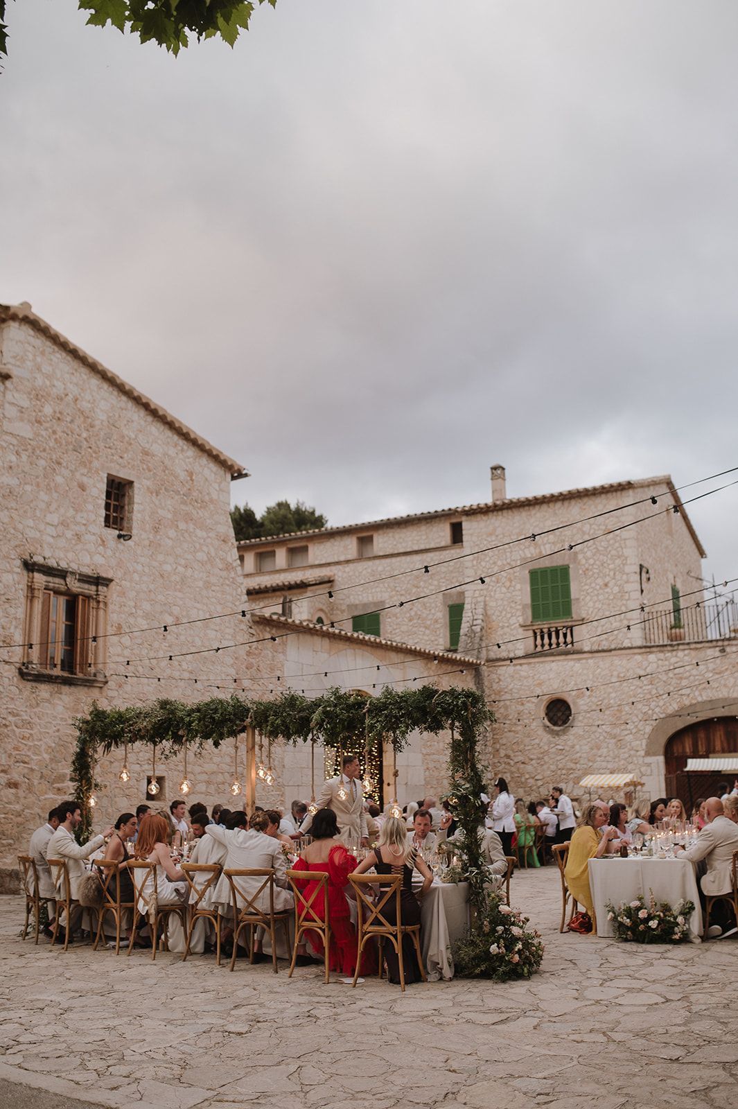 Elegant outdoor wedding dinner in a historic stone venue with string lights and floral arch.