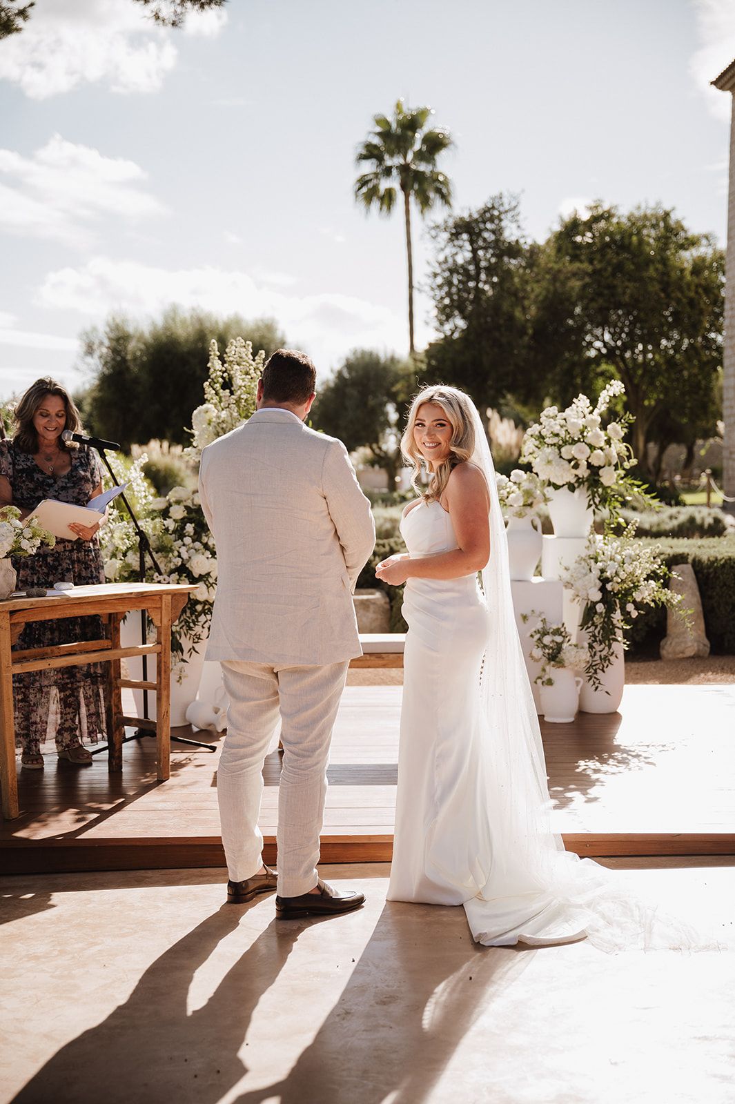 Bride and groom exchanging vows at outdoor ceremony with white floral arrangements.