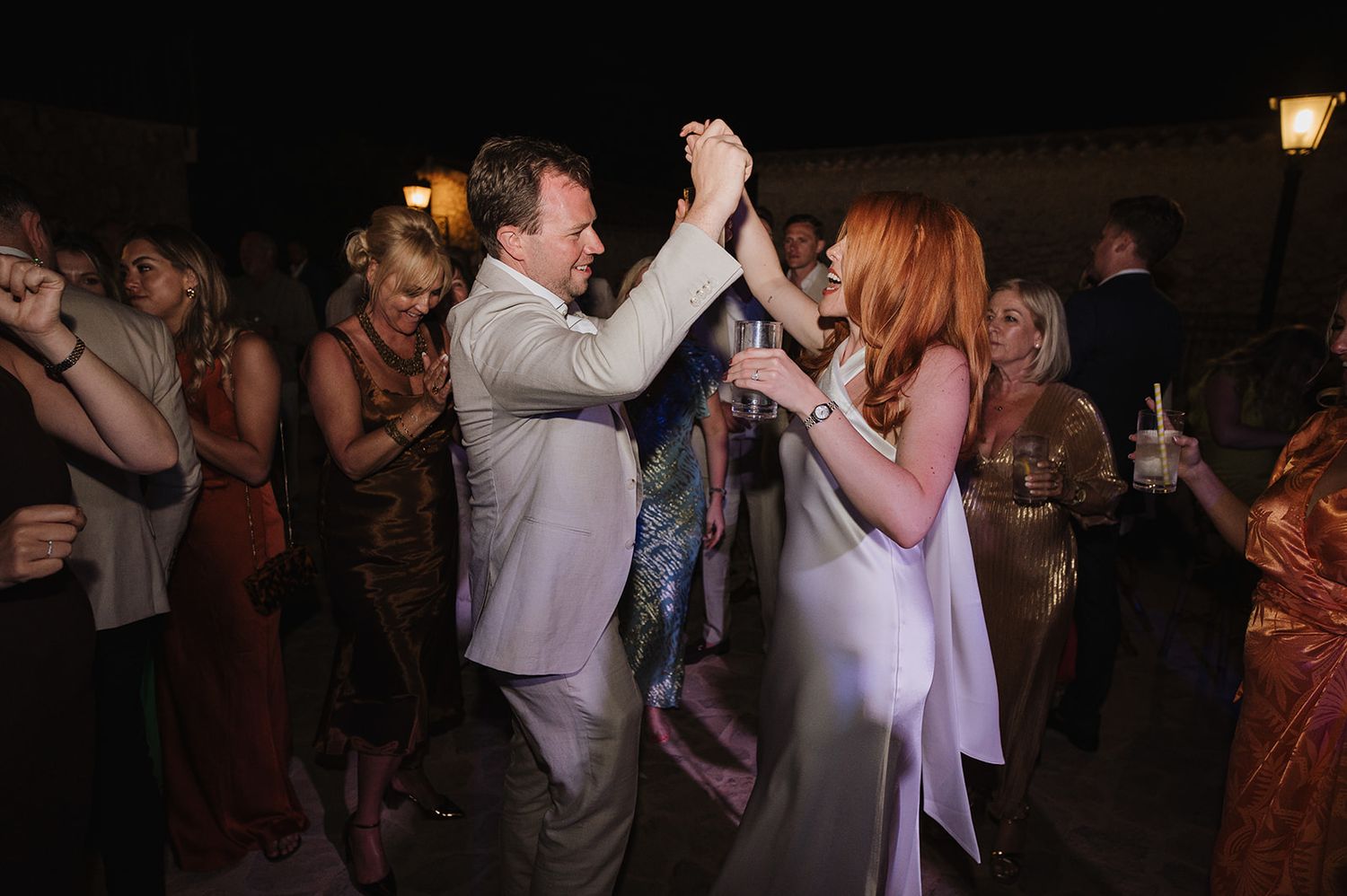 Couple dancing together hand in hand at an outdoor evening wedding celebration.