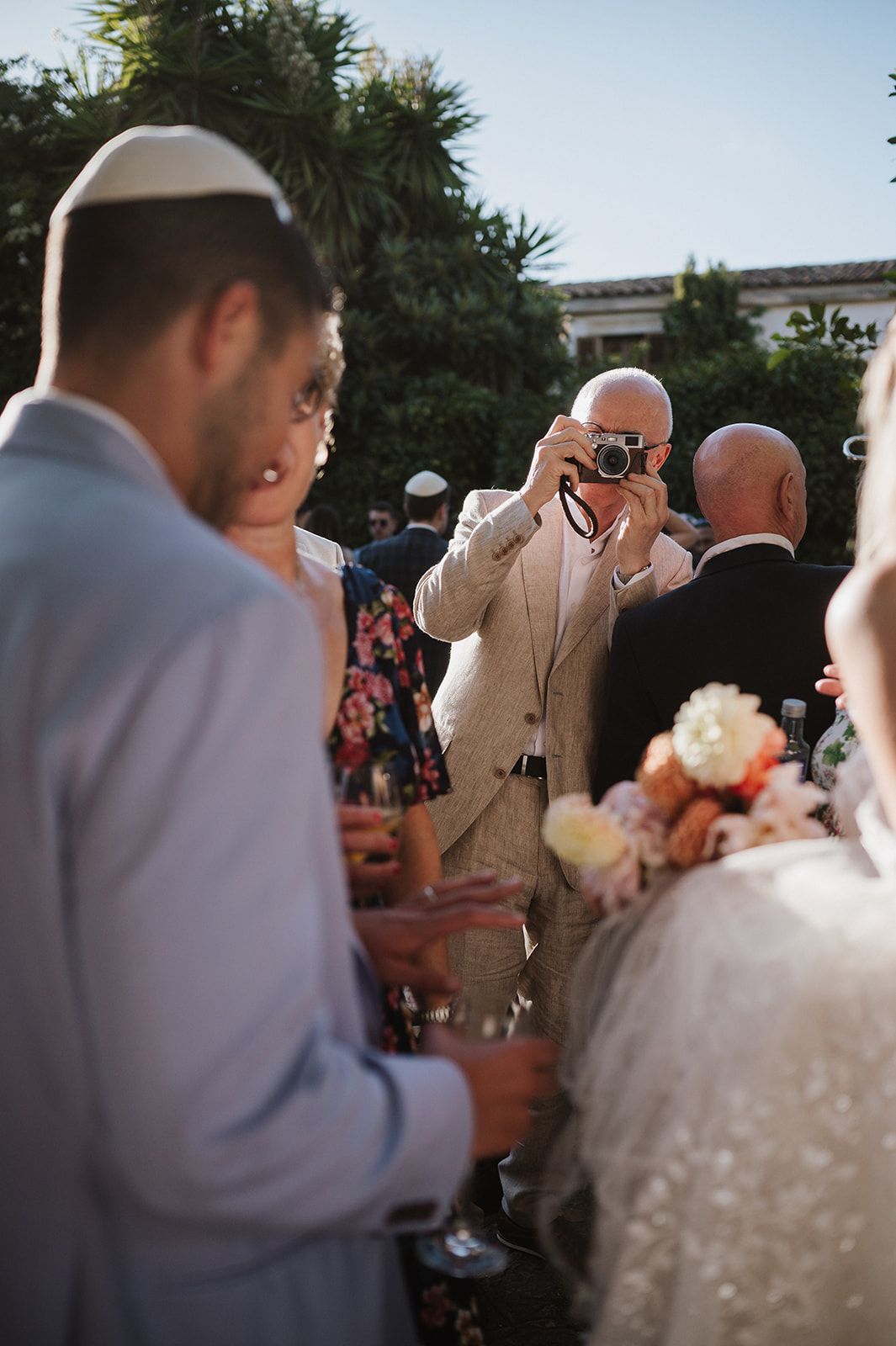 A guest photographs the bride and groom at an outdoor Jewish wedding ceremony.