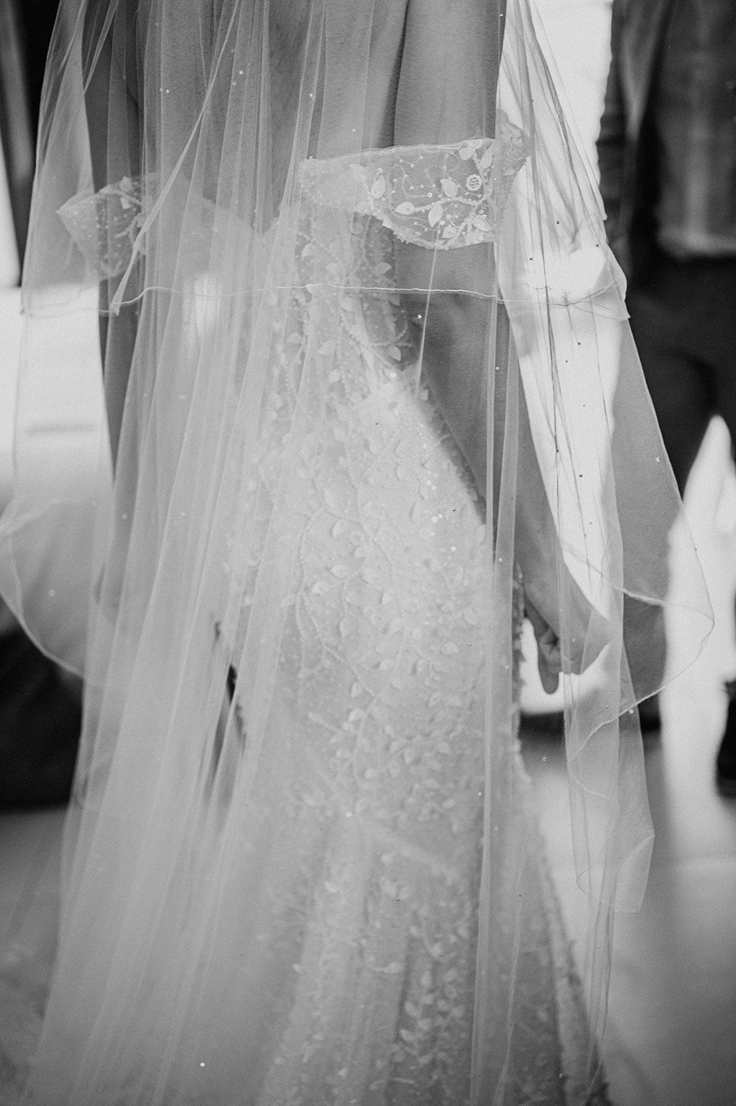 Black and white close-up of bride in intricate lace mermaid gown with delicate embroidered veil.