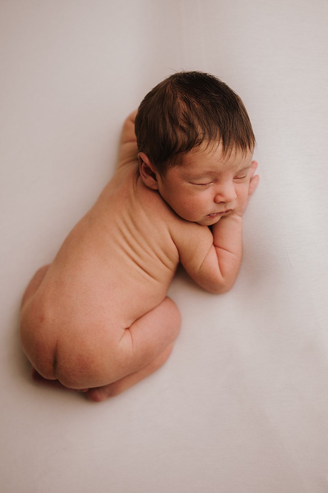 Peaceful newborn baby sleeping curled up on white background in classic newborn photography pose.