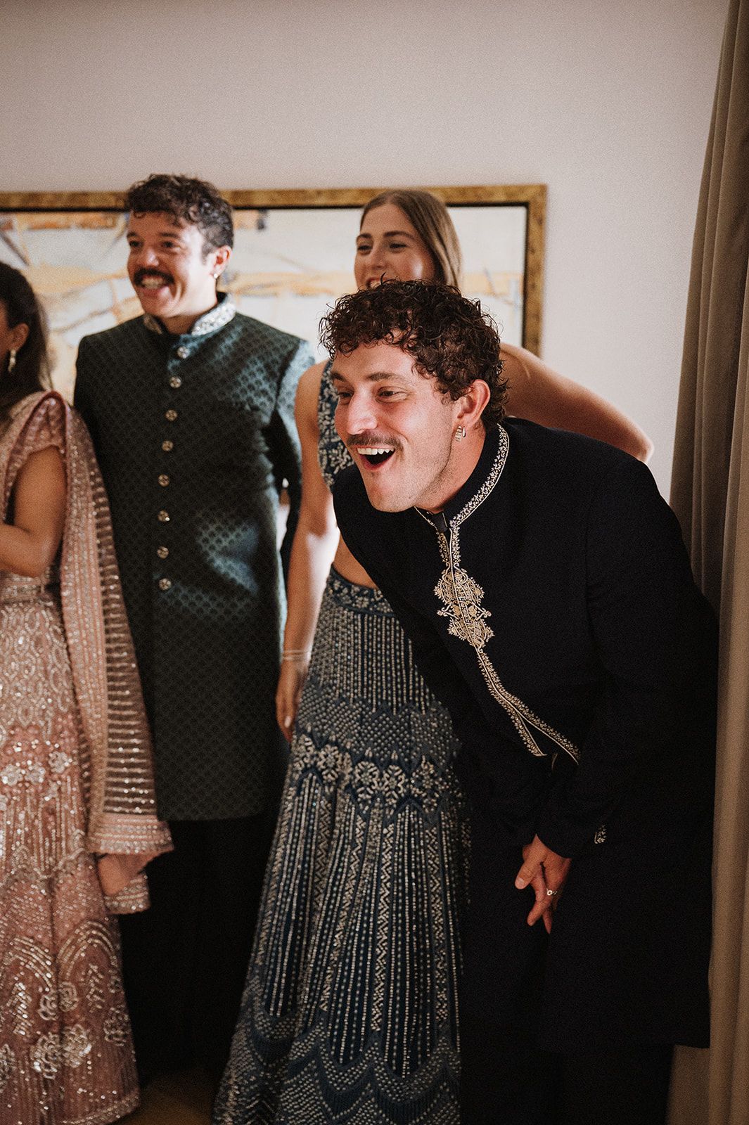 Guests laughing and celebrating in traditional Indian wedding attire at a festive indoor gathering.