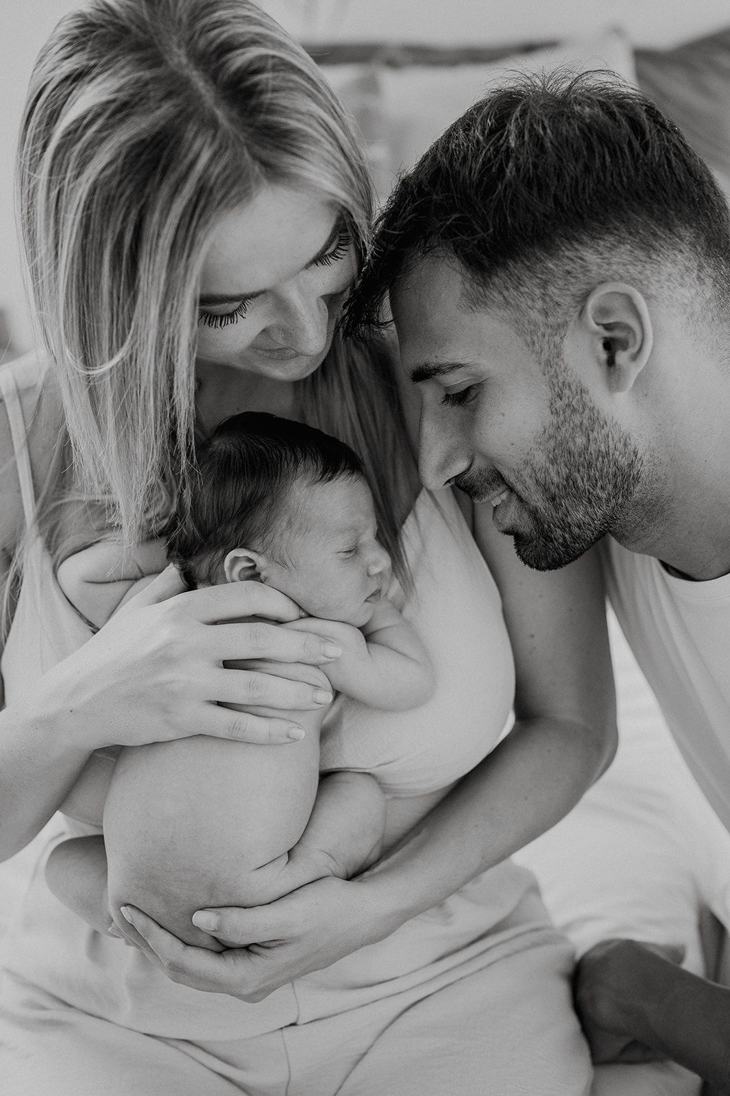 Black and white portrait of smiling parents tenderly holding their sleeping newborn baby close.