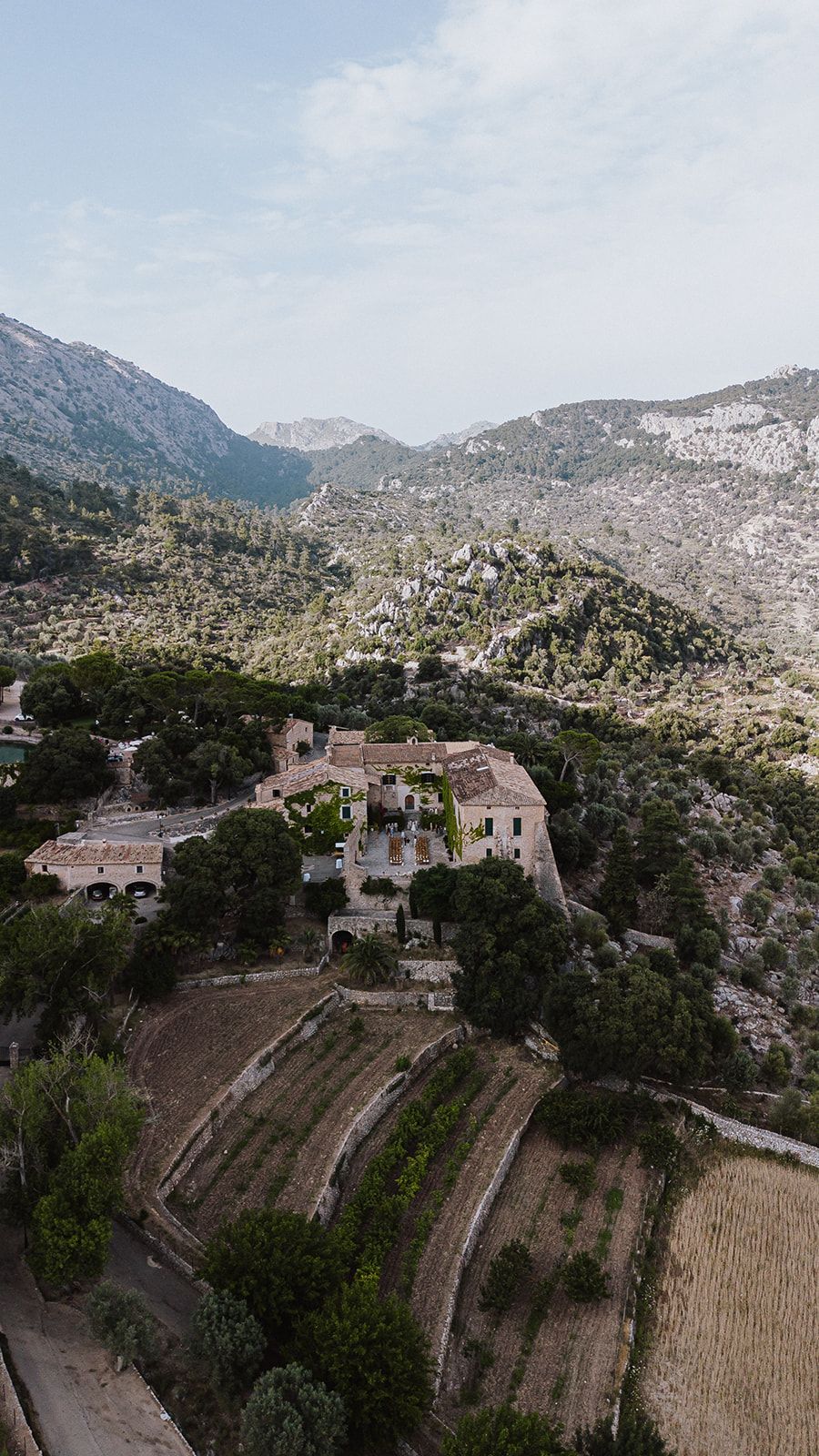 Aerial view of a historic stone estate nestled among terraced fields in a lush mountain valley.
