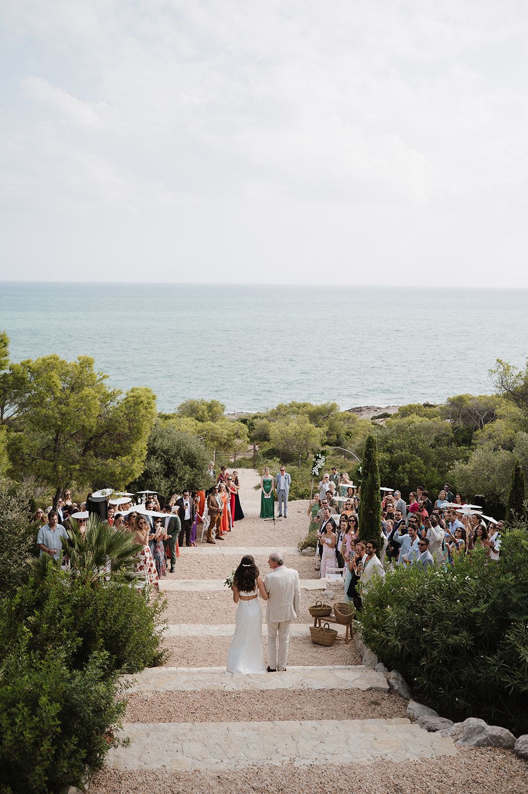 Aerial view of outdoor wedding ceremony on stone steps with ocean backdrop.