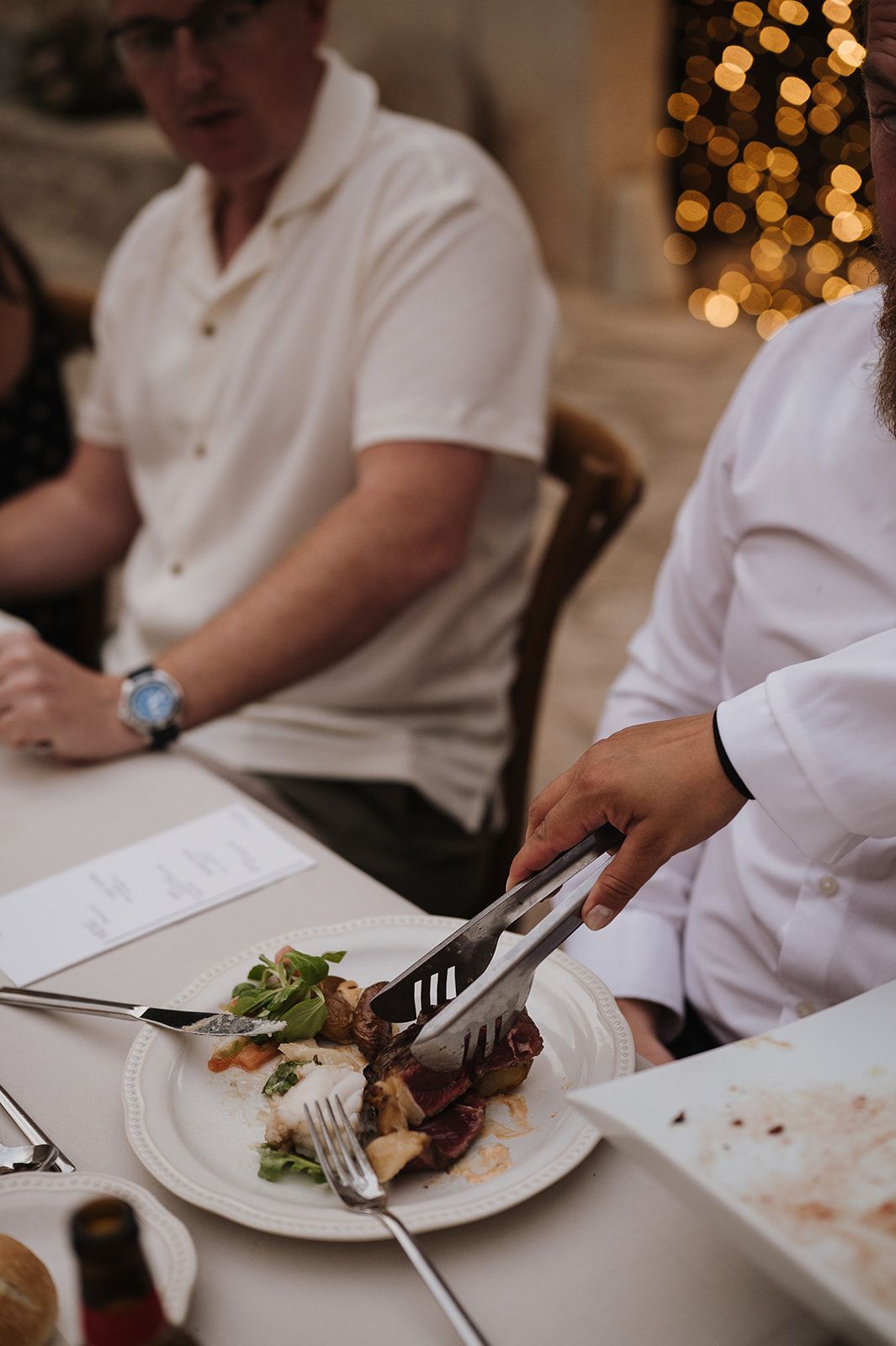 Chef serving food with tongs onto a white plate at an elegant dinner reception.
