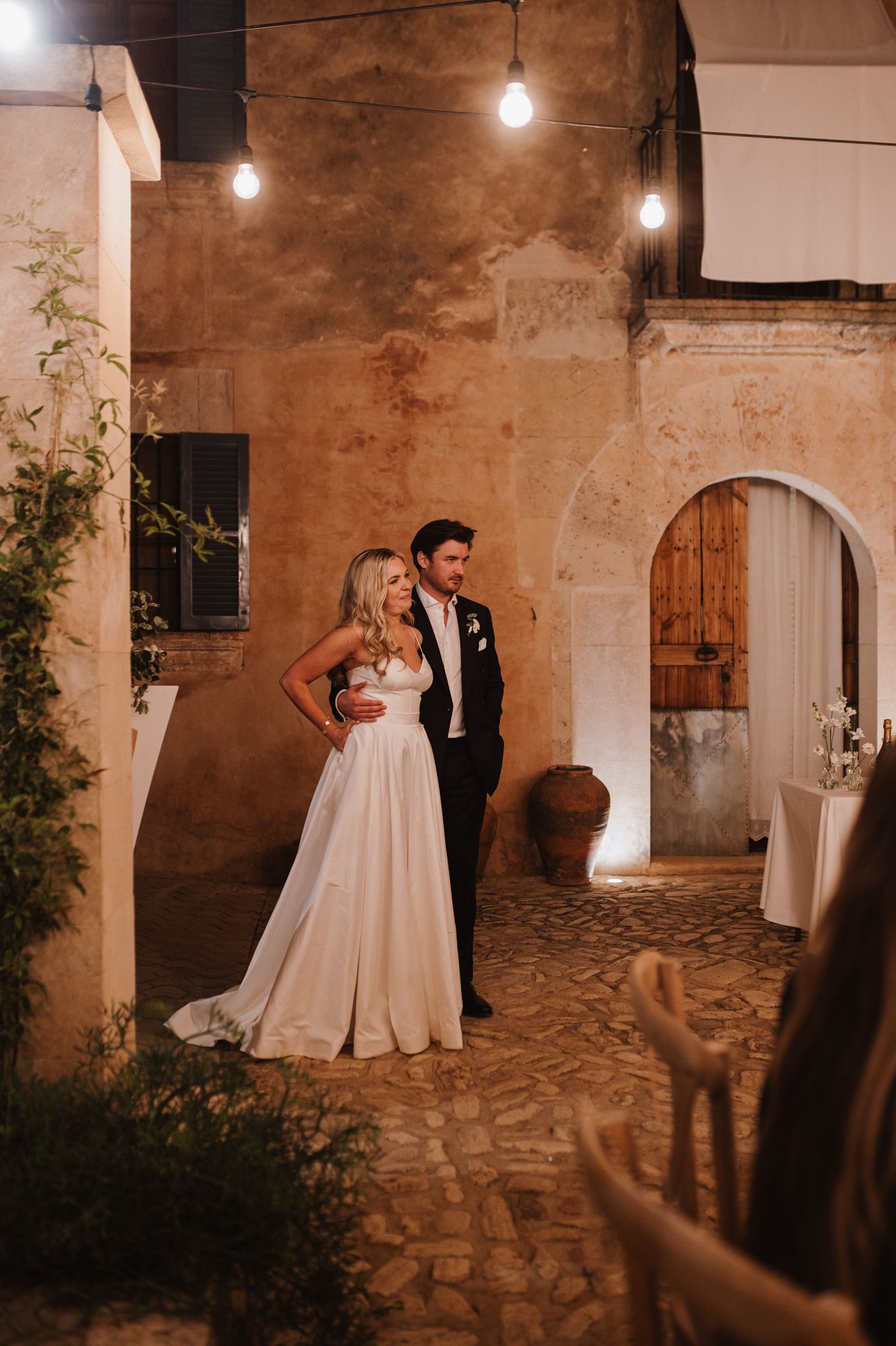 Bride and groom sharing a romantic moment in a warmly lit rustic stone courtyard at night.