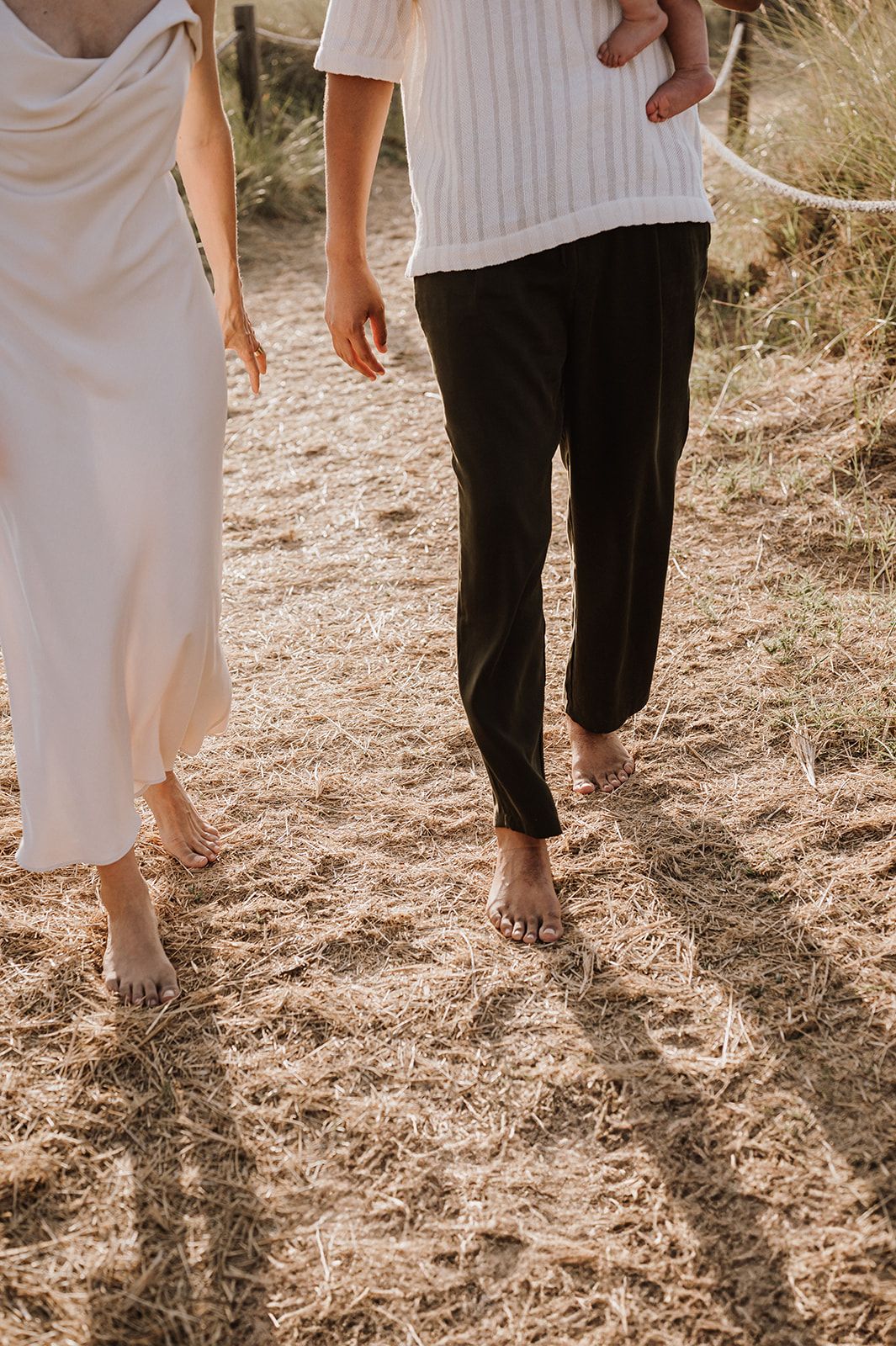 Barefoot couple walking together on dry grass at a sunny coastal location.