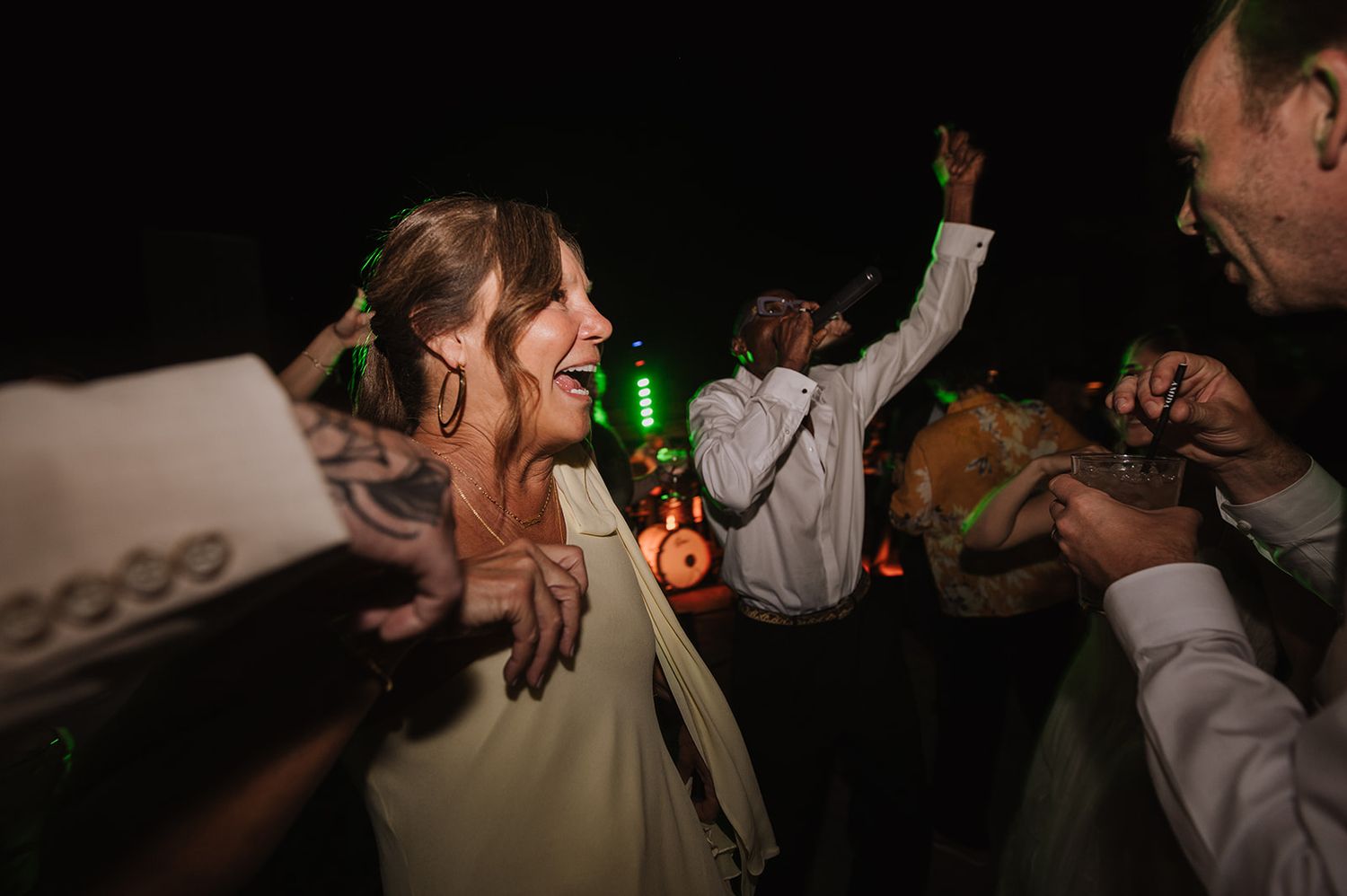 Joyful bride dances energetically with guests under green lights at a lively nighttime wedding reception.