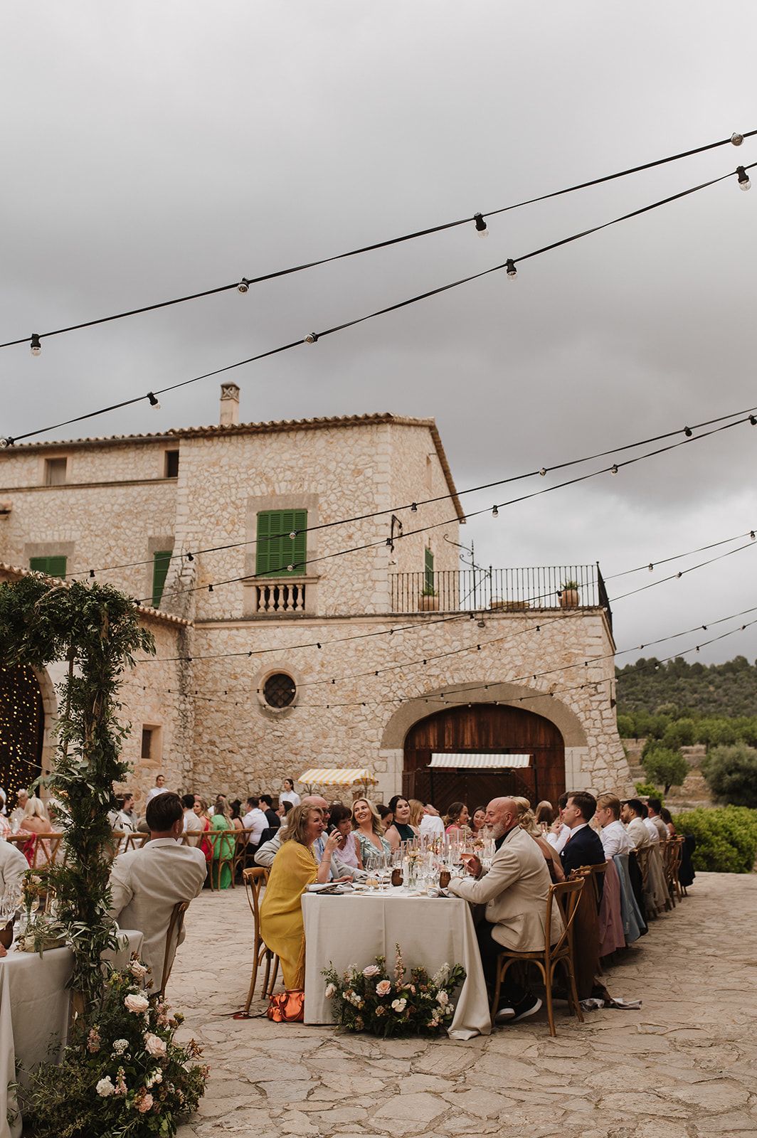 Aerial view of outdoor wedding reception at a rustic stone Mallorcan finca with long tables and string lights.